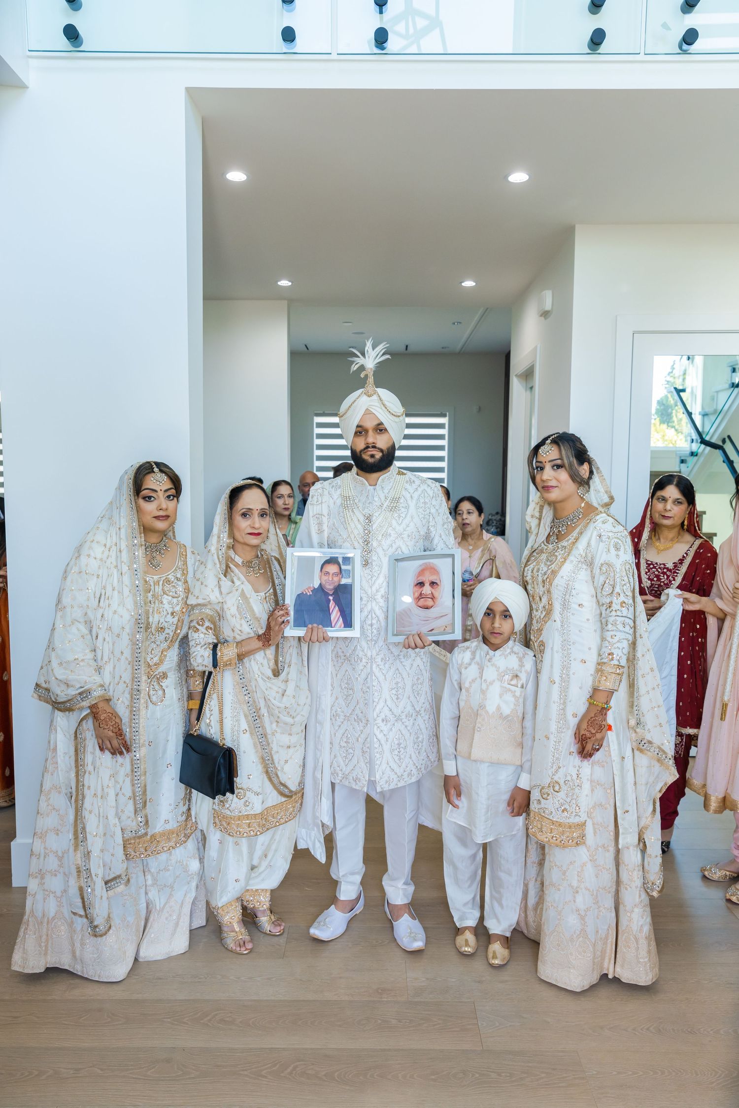 Wedding party members wearing matching white and gold traditional Indian outfits pose together indoors.