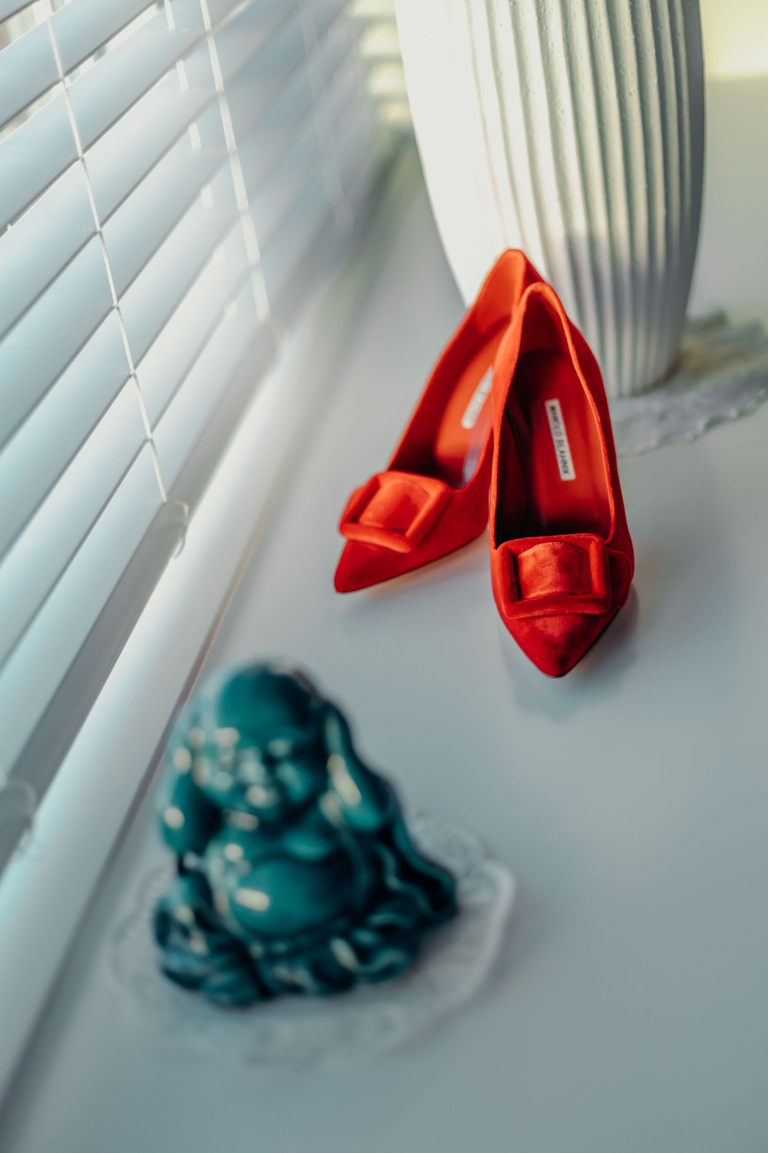 Red bridal shoes displayed against white window blinds with teal decor.