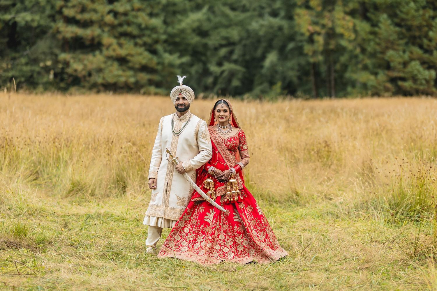 Couple in traditional wedding attire poses in a golden field during sunset.