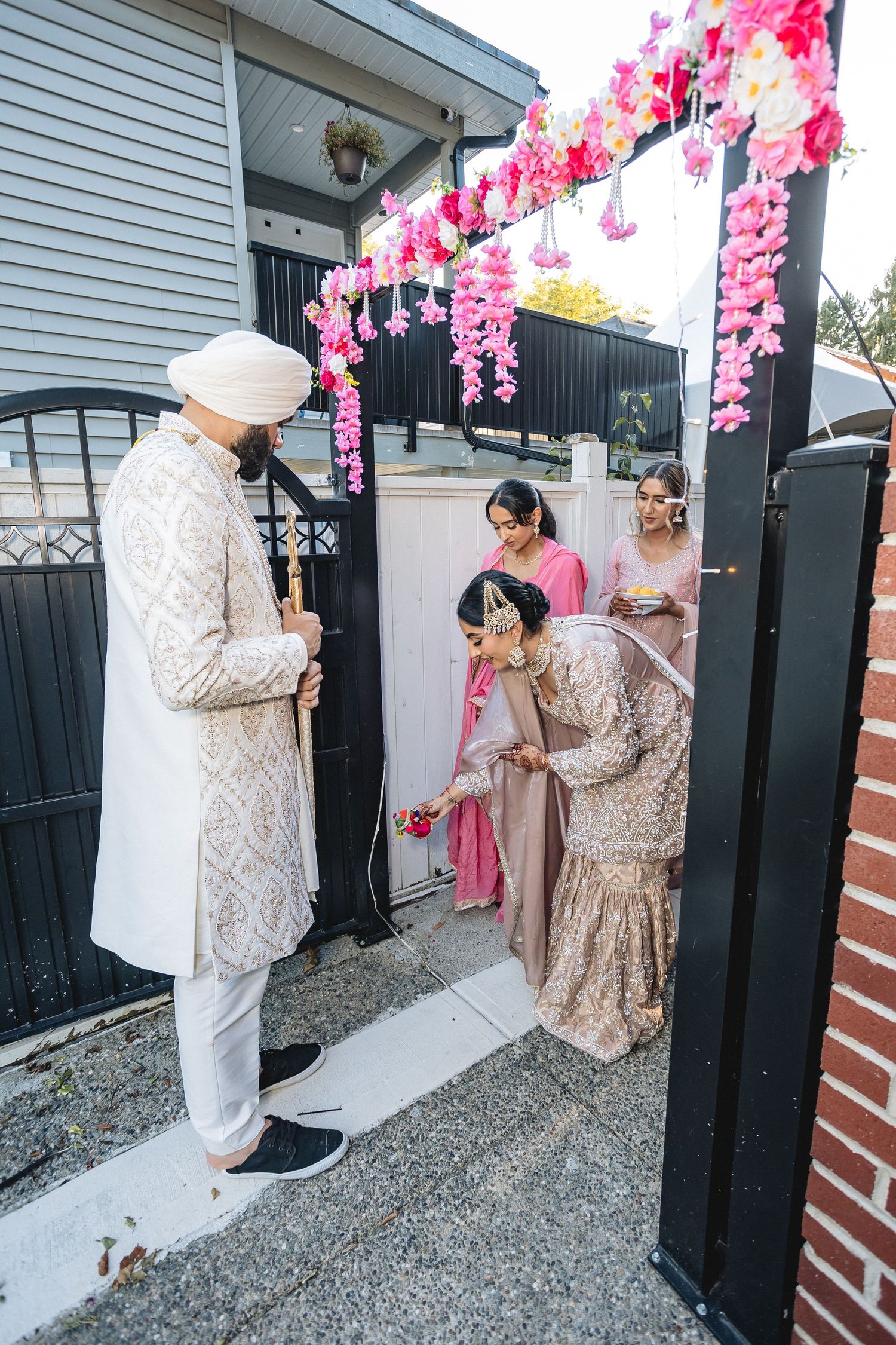 Wedding photo shoot outside a house with pink floral decorations and black gates.