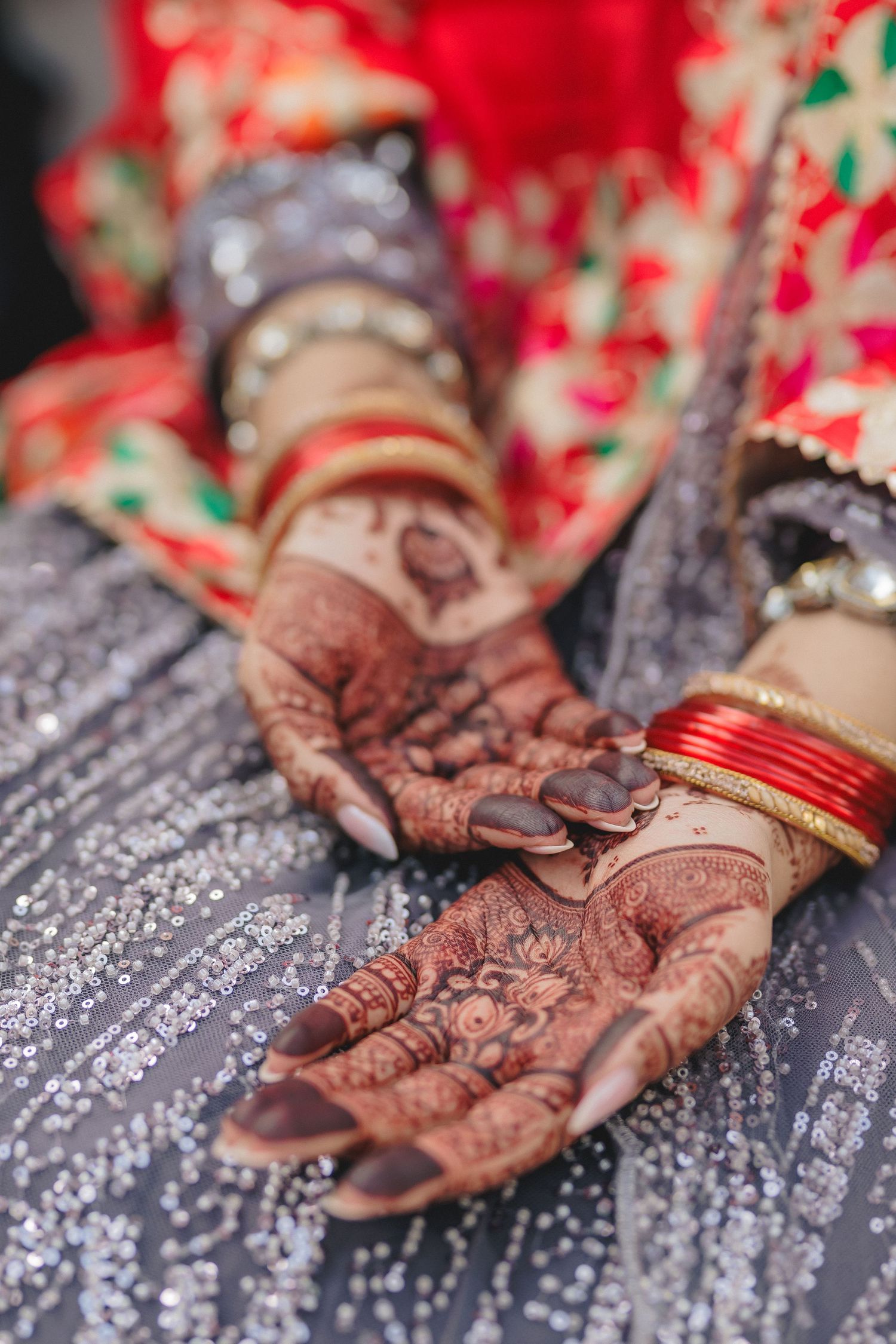 Detailed mehndi designs on hands with traditional red and gold wedding bangles.
