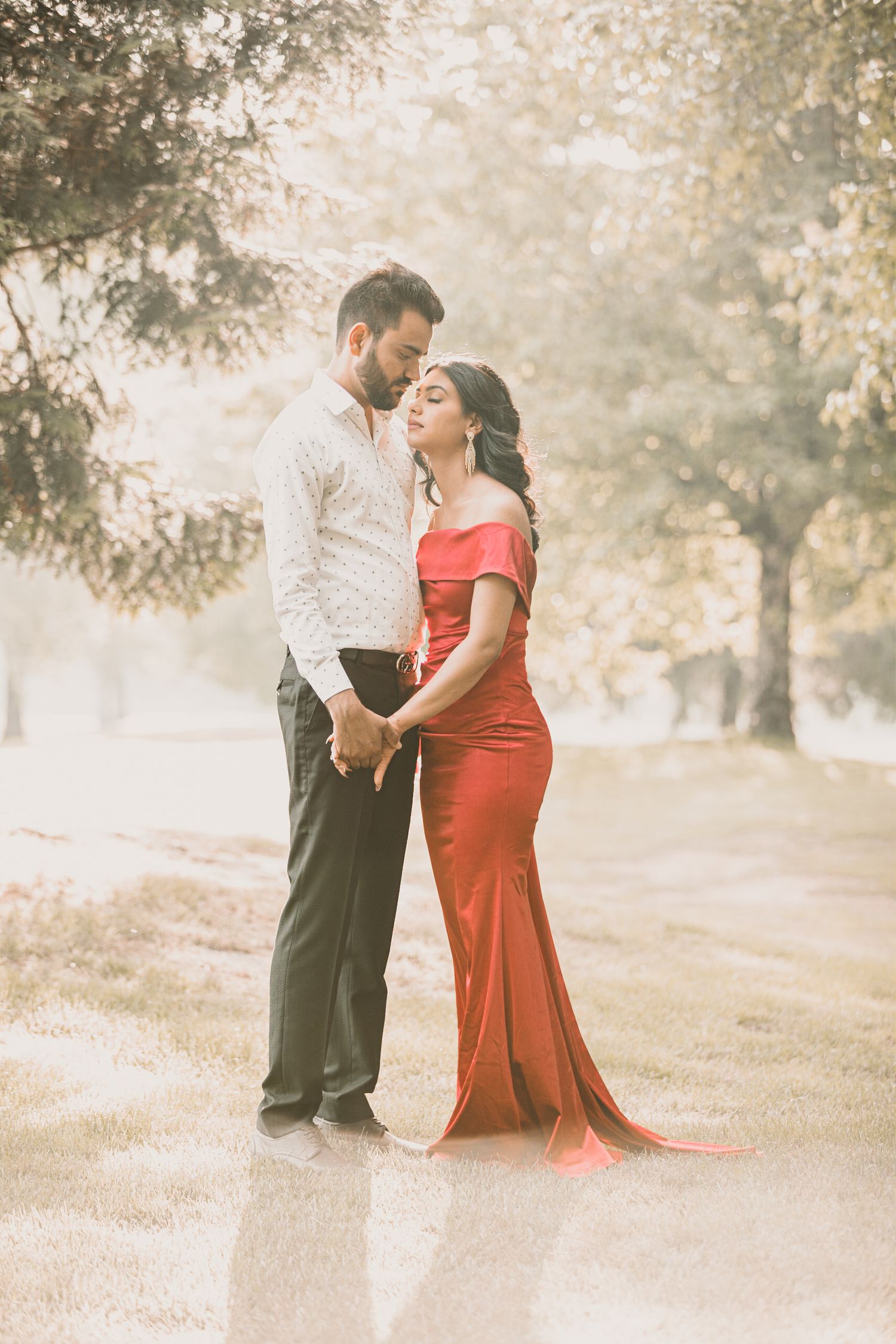 Romantic couple photoshoot in a misty park with person in red dress and formal attire.