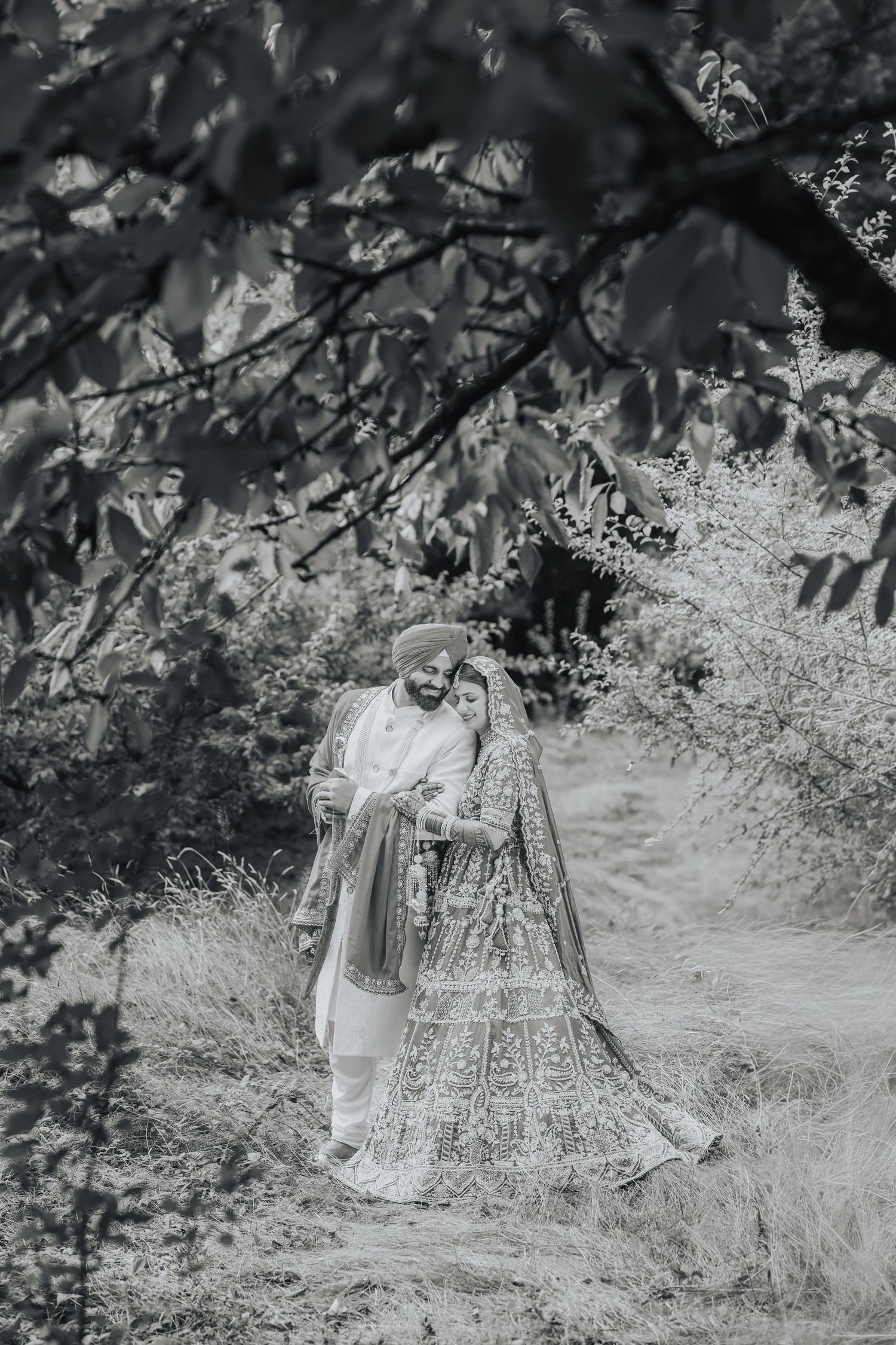 Black and white photo of a couple in traditional wedding attire walking through a garden path.