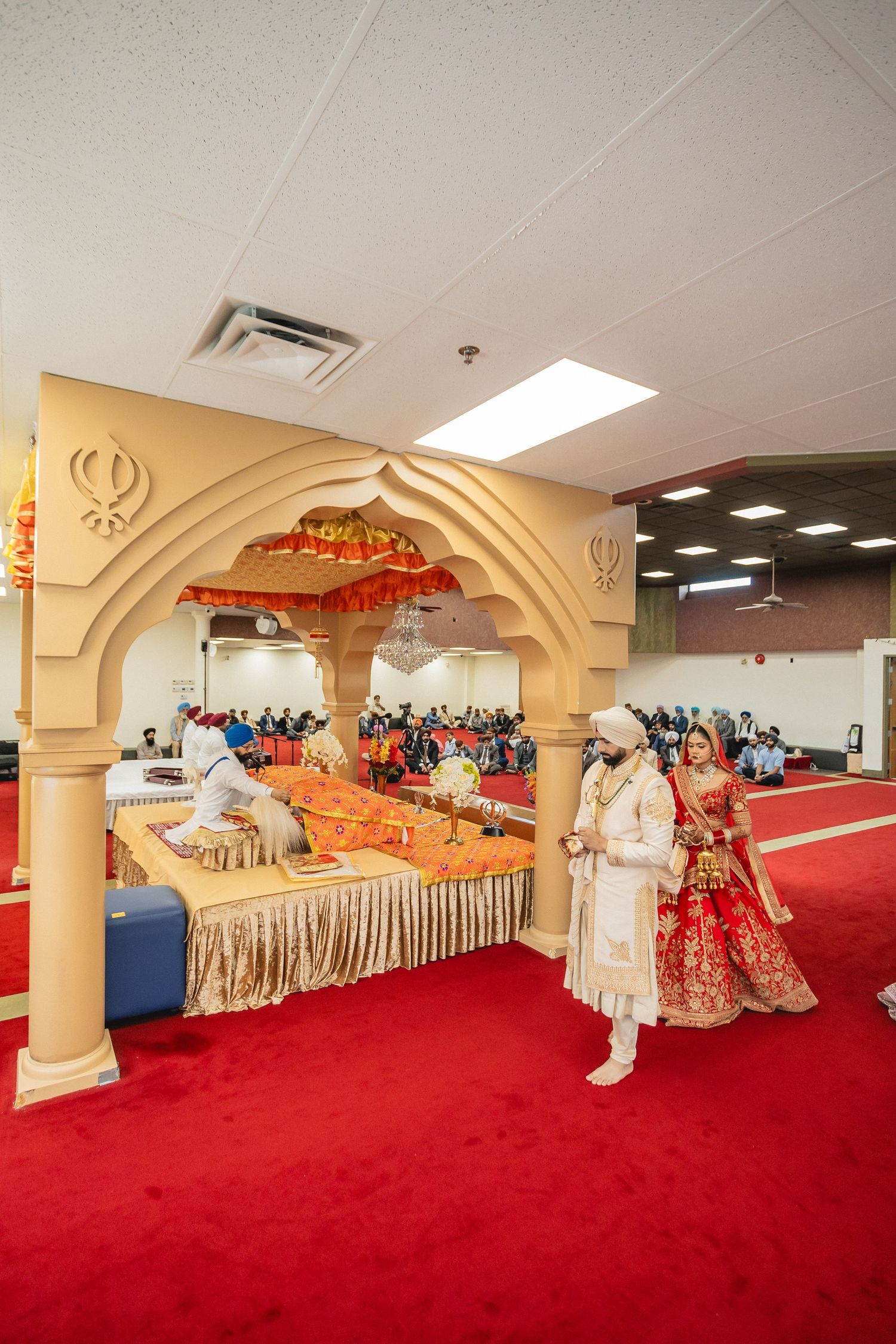 A wide view of a Sikh temple interior with red carpeting and ornate archways.