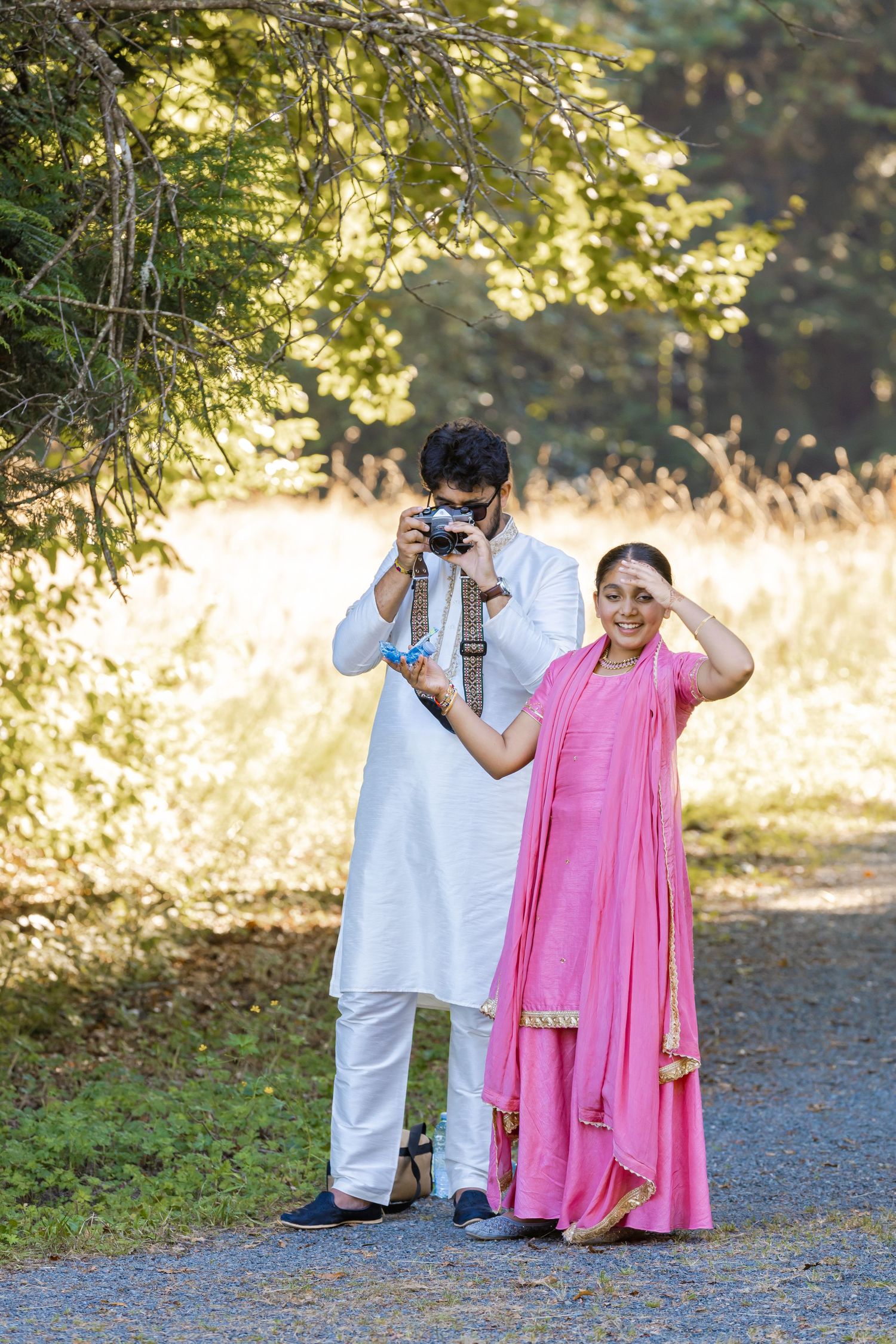 Playful photo session in a park with subjects in white and pink outfits using cameras.