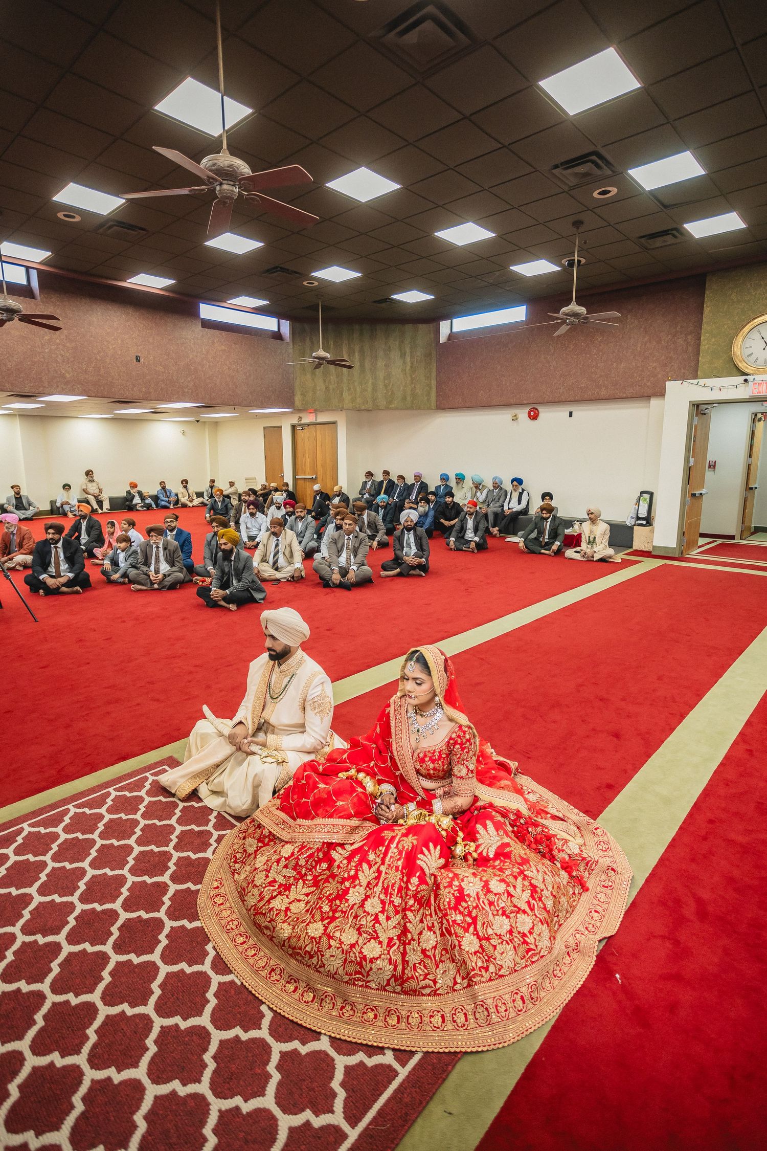 Wedding ceremony in large hall with red carpet and geometric pattern design.