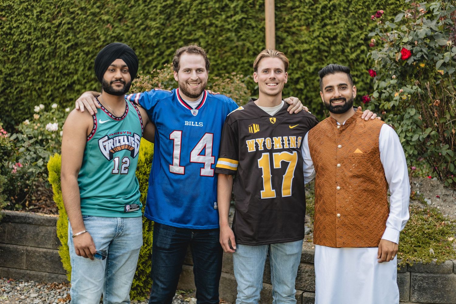 Four friends pose together, mixing casual sports jerseys with traditional South Asian clothing in a garden.