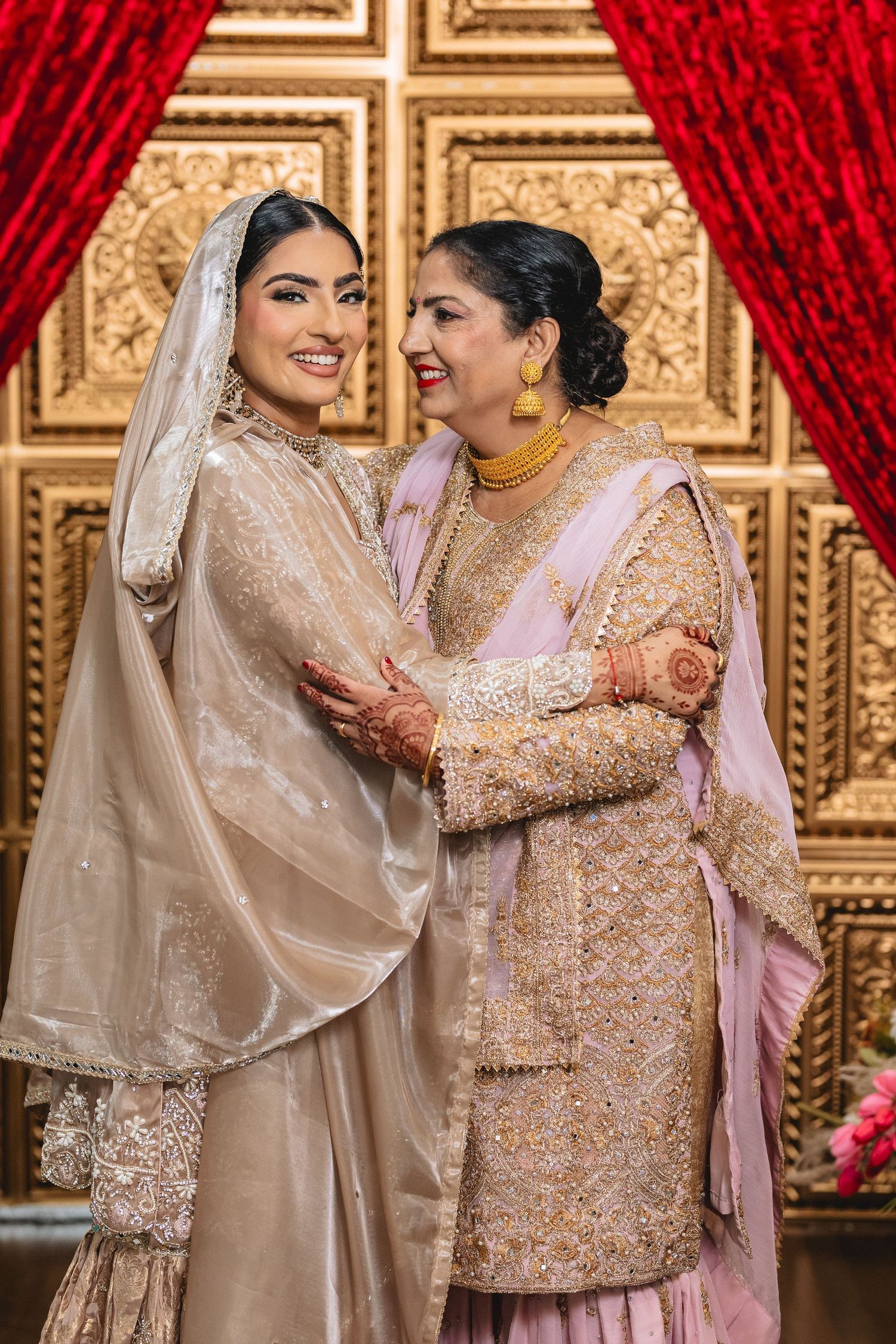 Two people in shimmering beige and pink traditional outfits share a joyful moment.