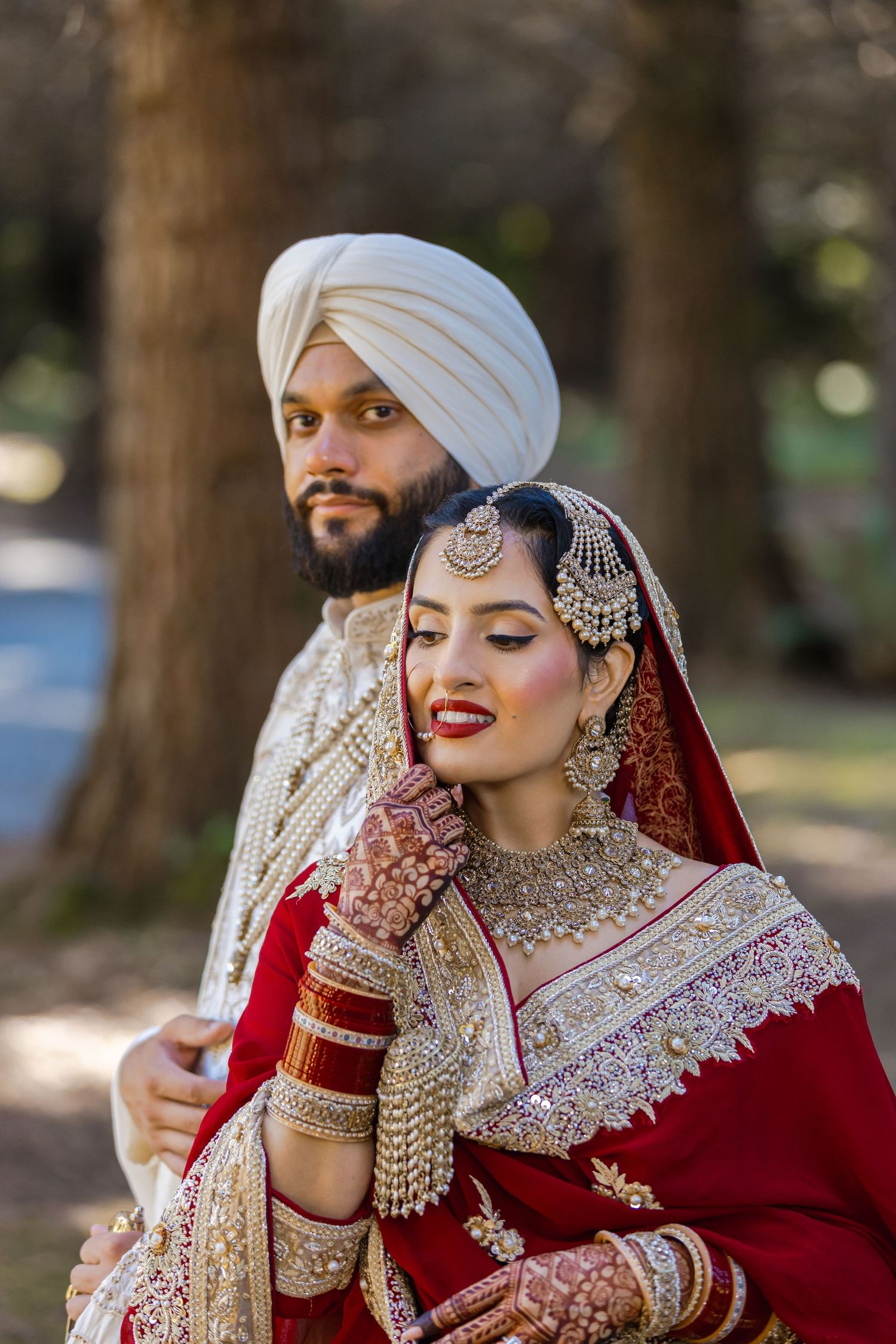 Elegant couple in traditional Sikh wedding attire pose together outdoors.