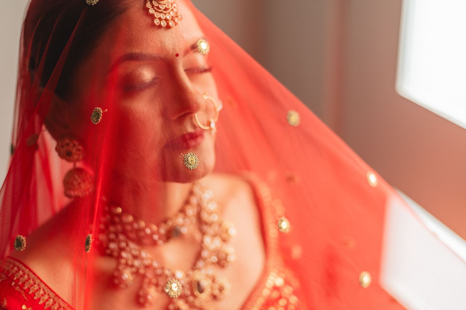 Indian bride wearing traditional red wedding attire with ornate gold jewelry and henna adorned hands.
