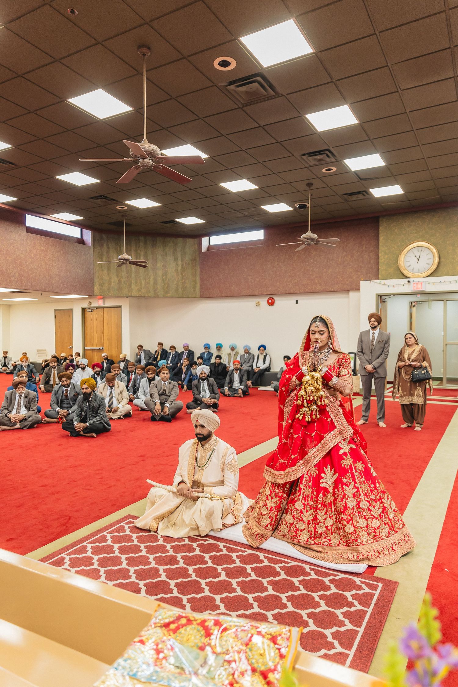 Wide view of Sikh wedding ceremony in indoor venue with red carpet and seated guests.