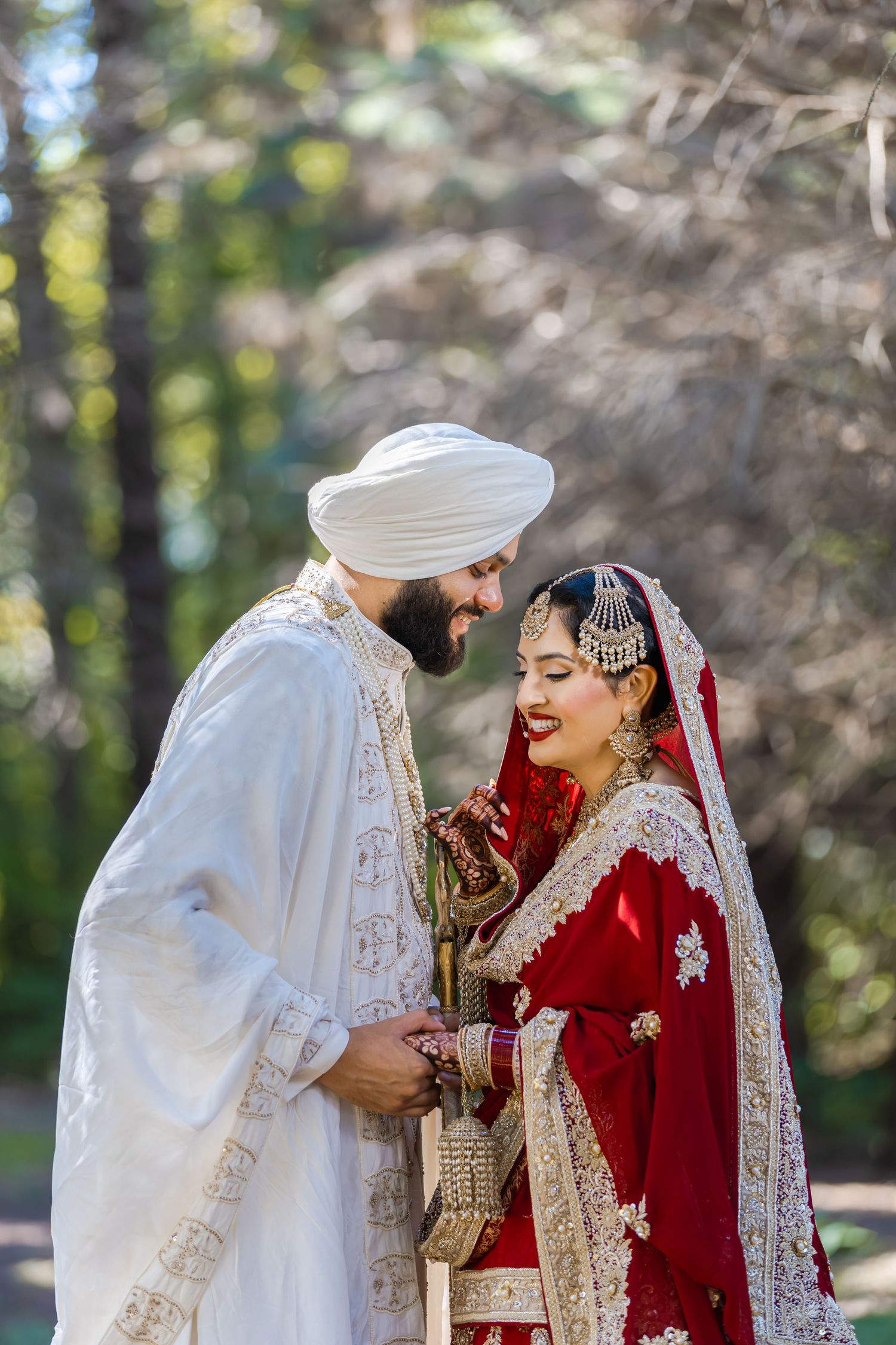 Wedding couple in traditional red and white attire pose together in an outdoor forest setting.