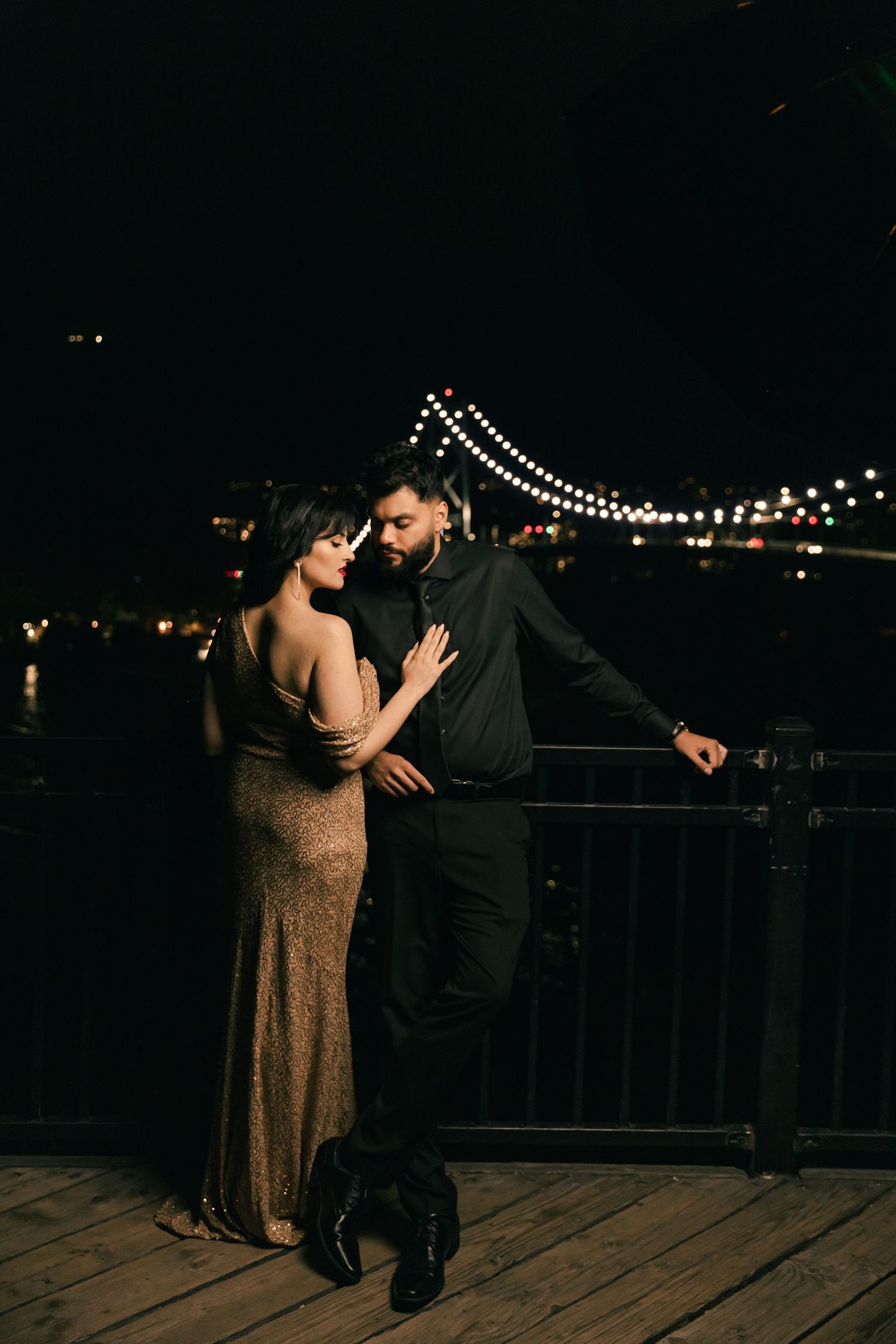 Couple dancing intimately on a wooden deck at night with string lights in the background.