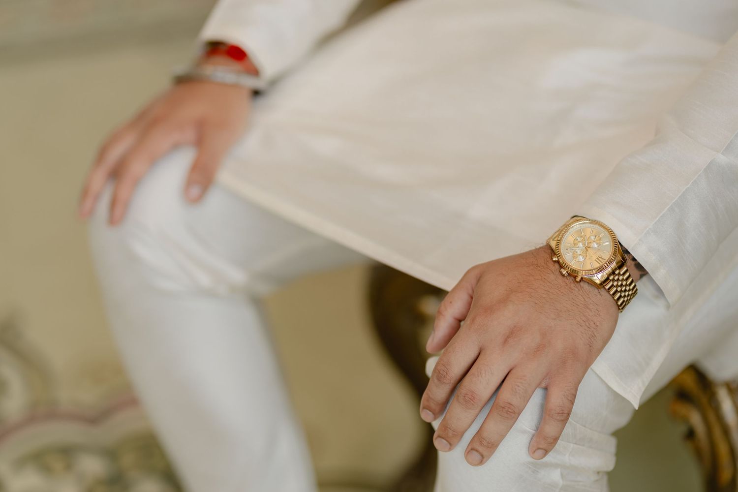 Close-up of hands wearing gold watch against white formal attire.