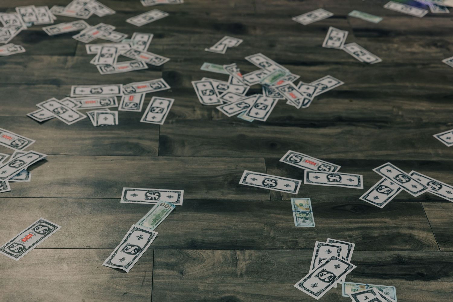 US dollar bills scattered across a dark wooden floor surface.