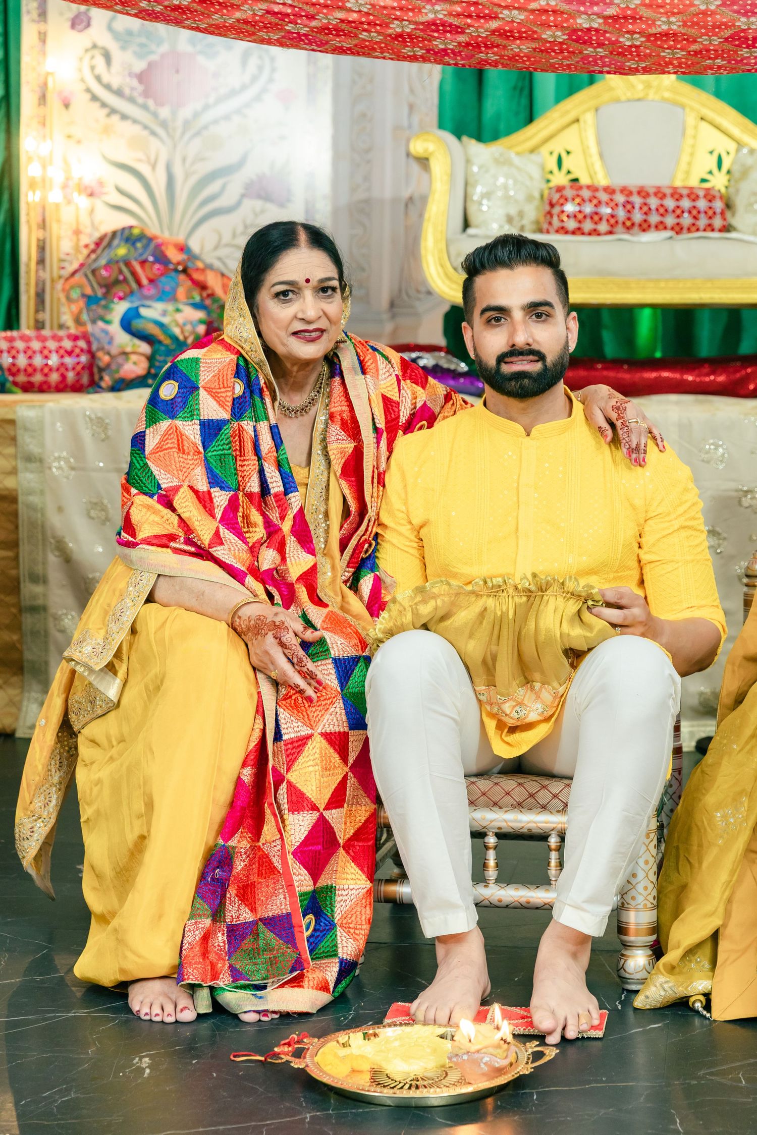 A couple in coordinating yellow and colorful outfits pose together on a dark floor.