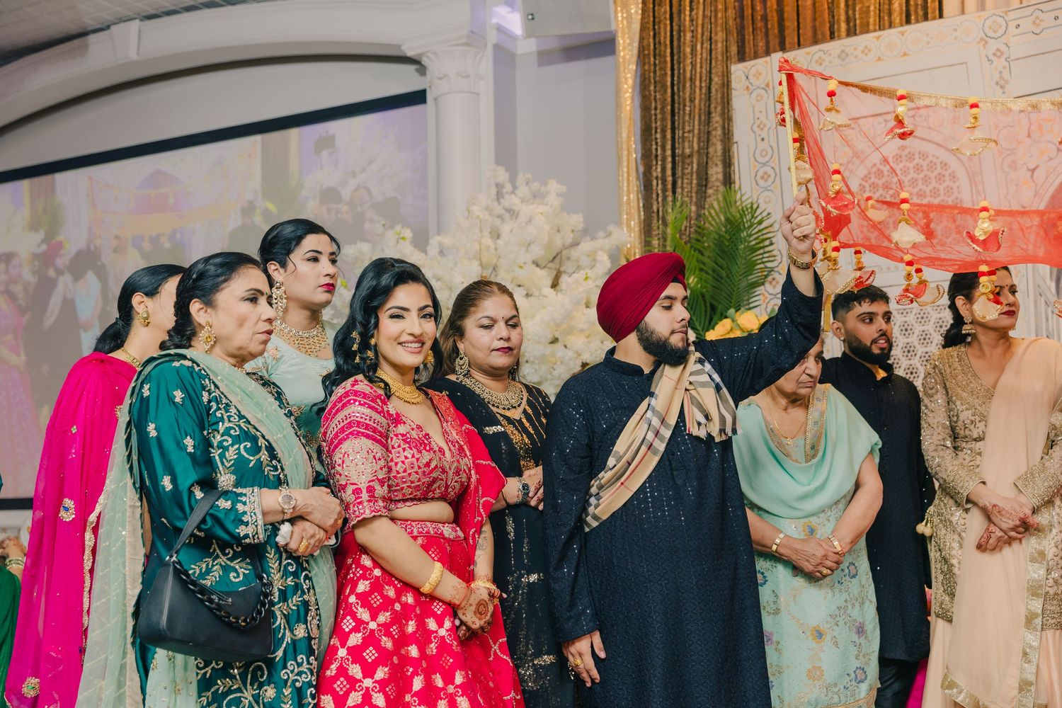Wedding guests in colorful traditional Indian outfits gather for group photos at a celebration.