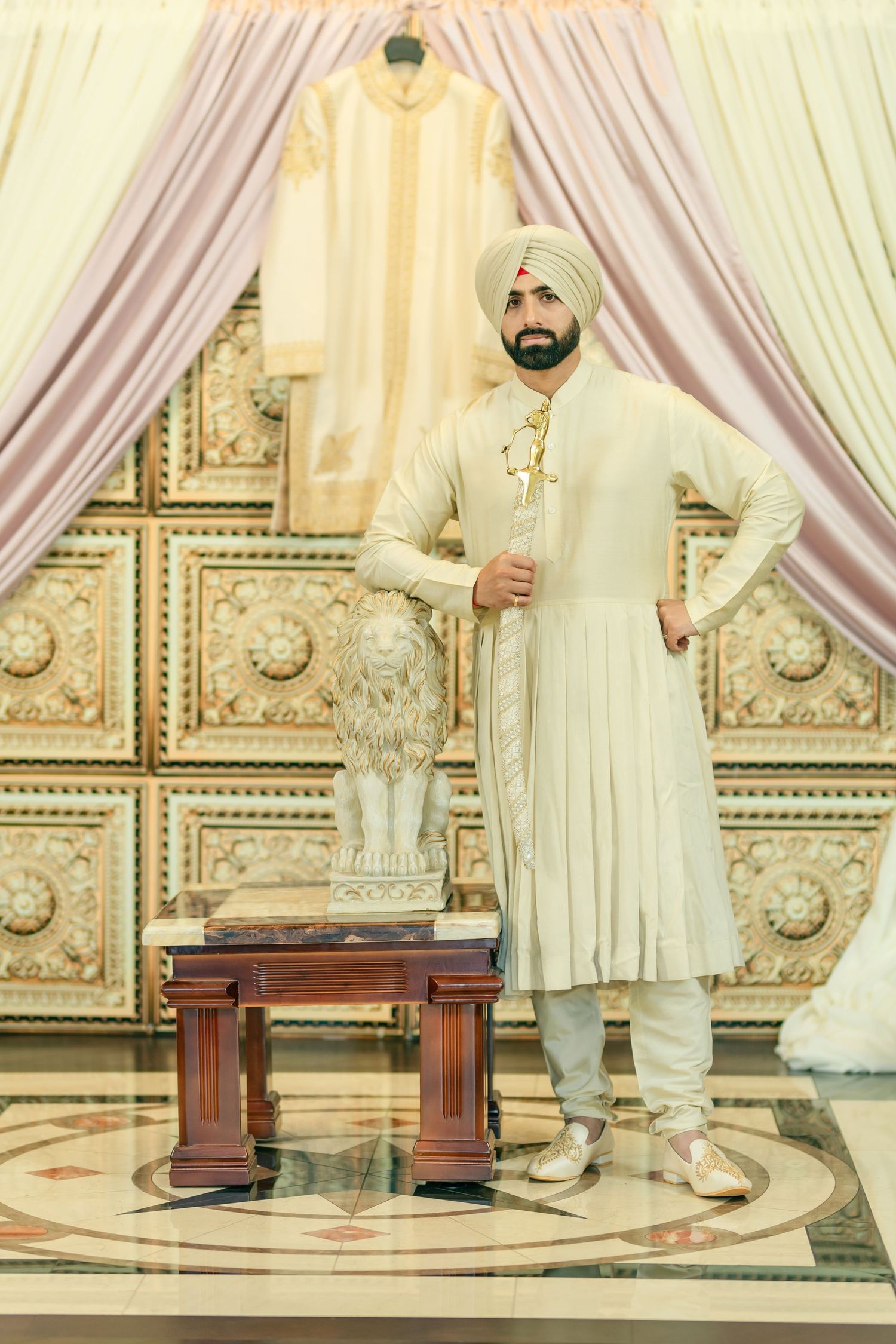 People in cream-colored traditional attire pose on an ornately decorated stage with draped fabric.