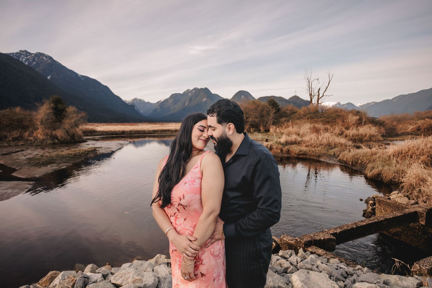 A couple shares an intimate moment by a scenic mountain lake during sunset.