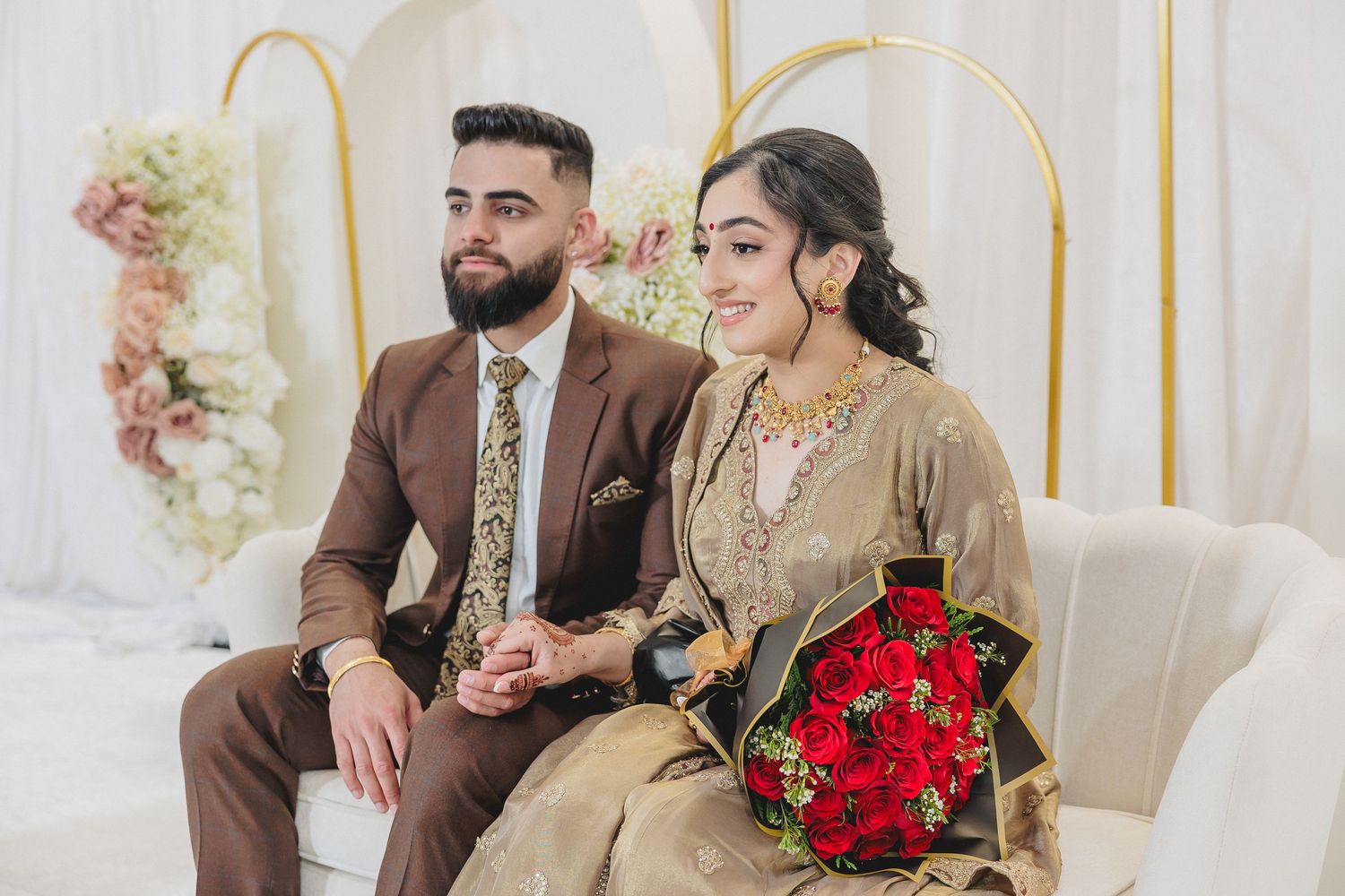 Couple seated on an elegant white sofa with gold accents and floral decorations.