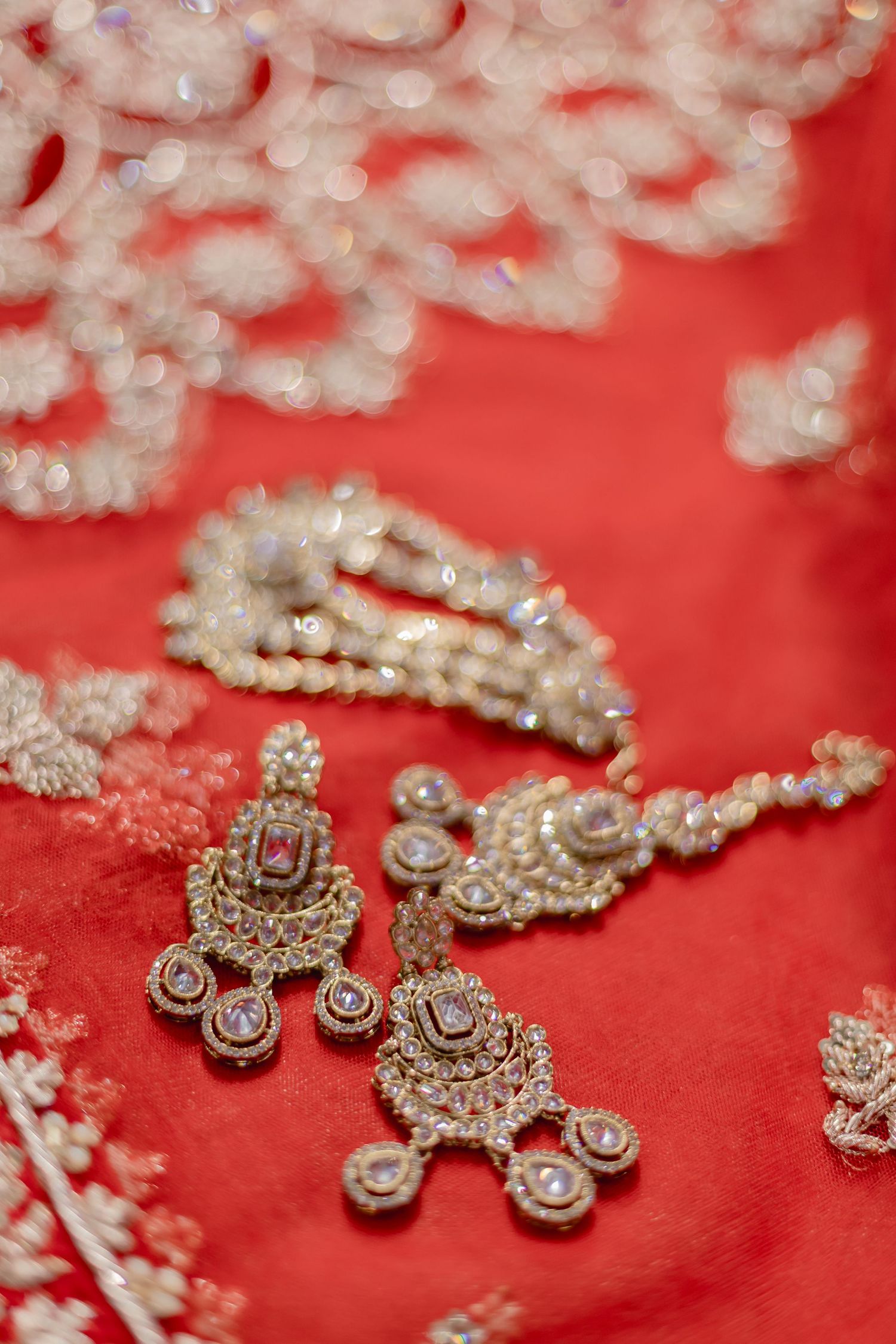 Ornate crystal and gold wedding jewelry displayed on red fabric with delicate lace details.