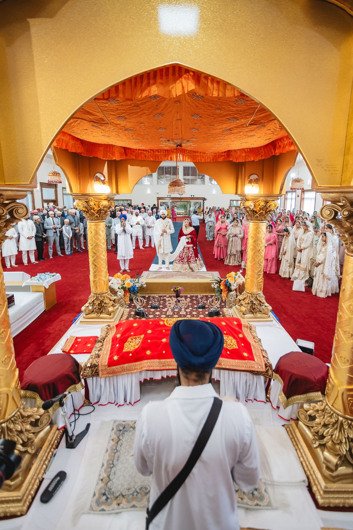 Interior view of a Sikh temple ceremony space with red carpeting and ornate decorations.