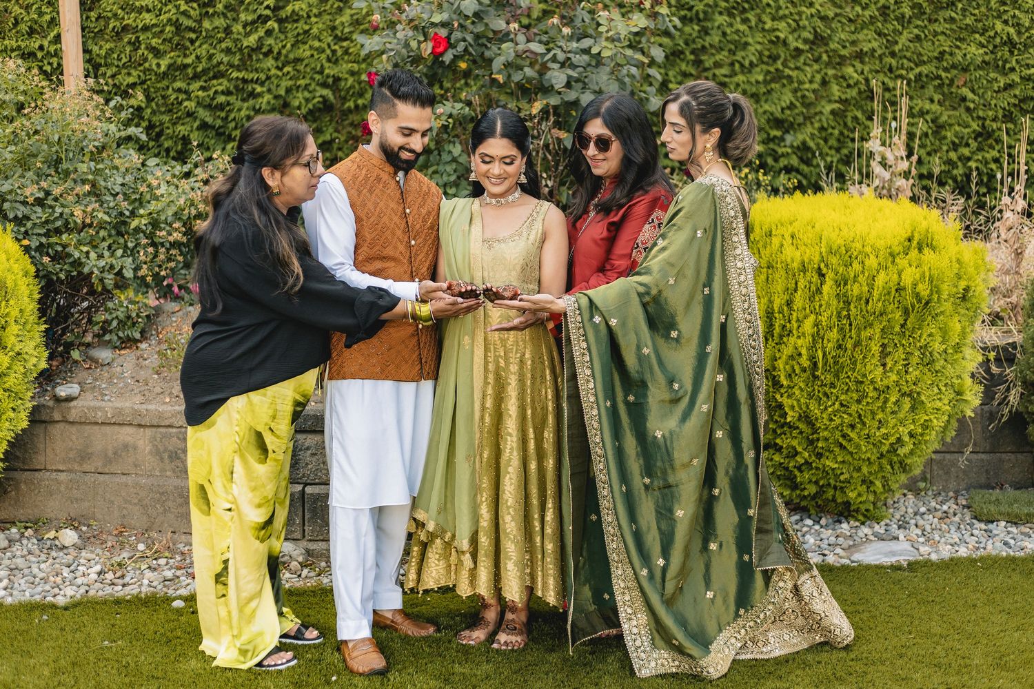A small group wearing colorful traditional Indian outfits gathers in a garden setting.