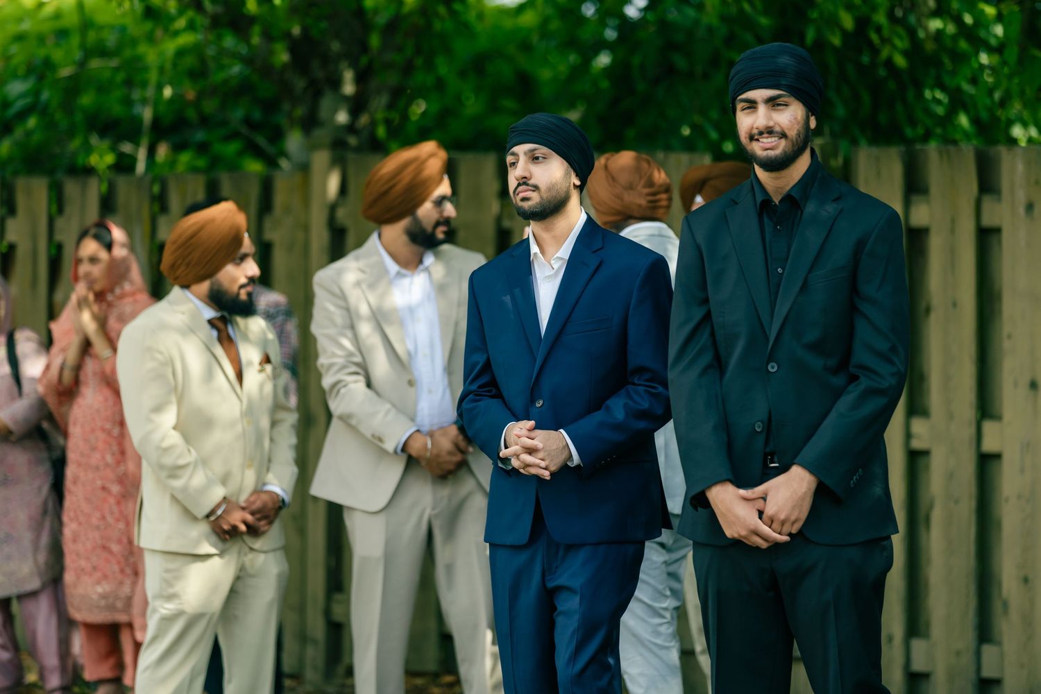 Group wearing formal attire stands together outdoors during special event.