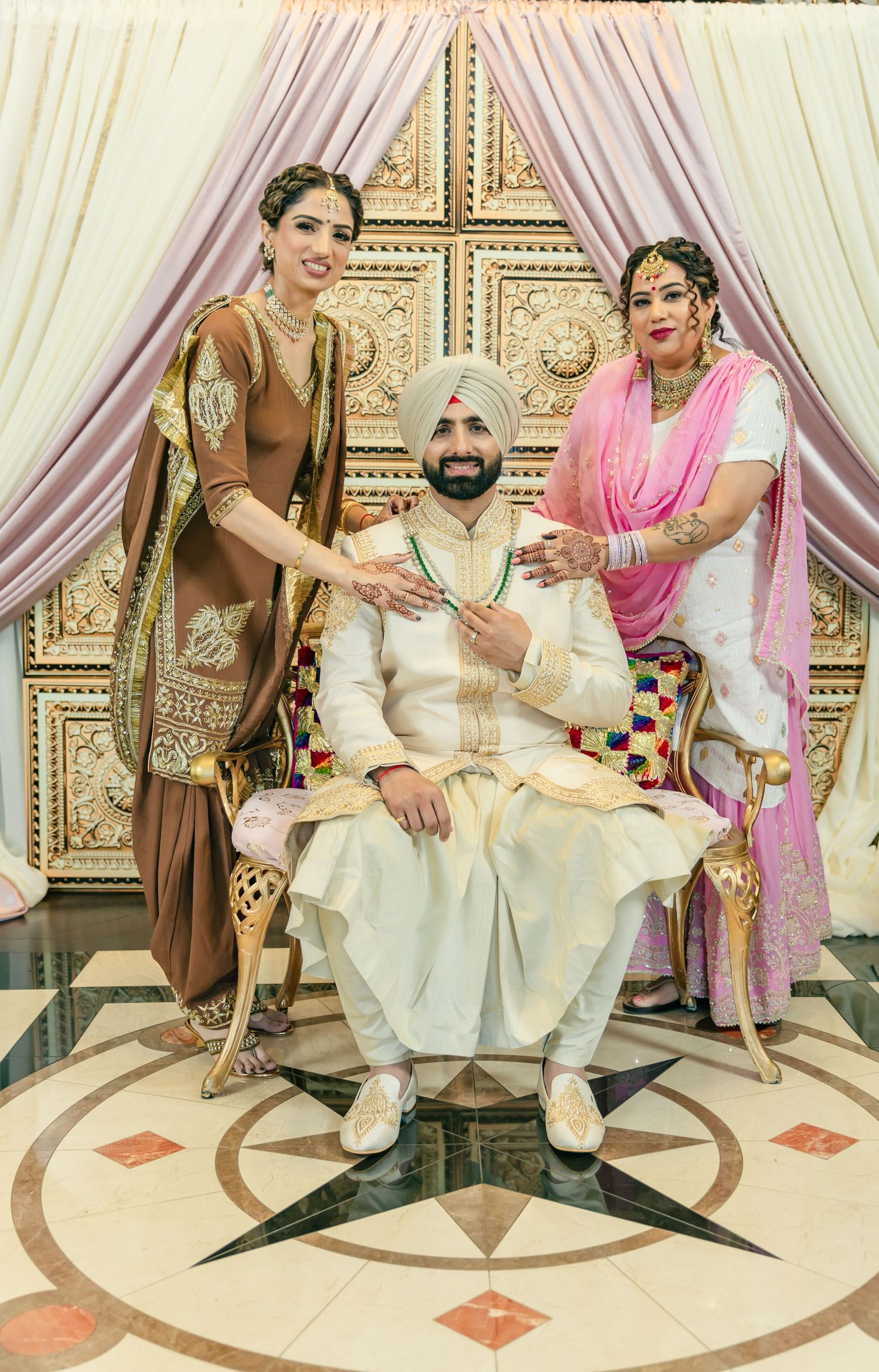 Wedding party seated on ornate chairs with gold and white decor during traditional Indian ceremony.