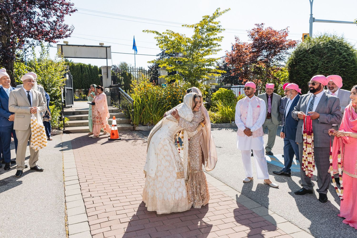 Wedding procession with guests in traditional Indian attire walking along outdoor pathway.