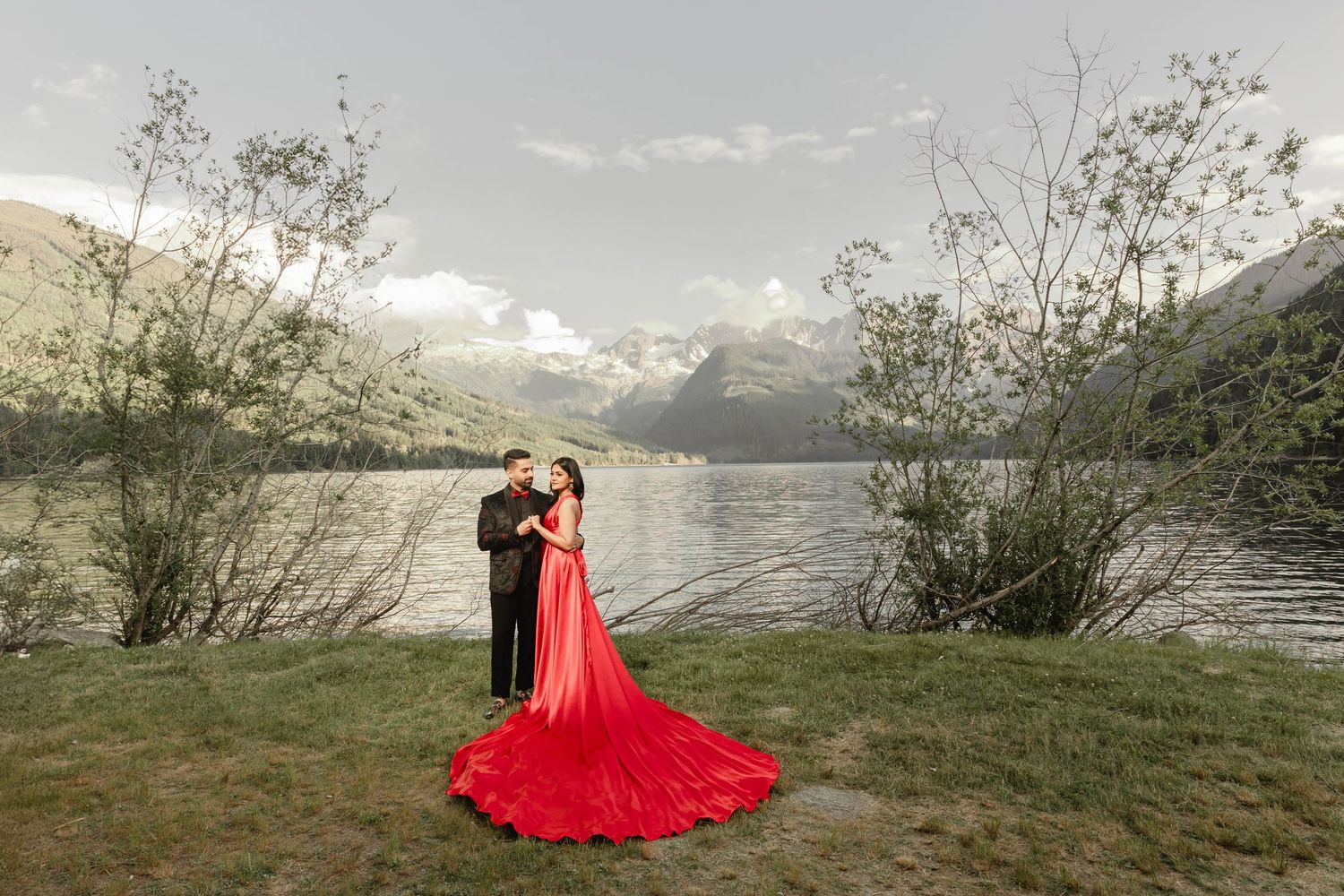 A dramatic red dress flows across a scenic mountain lakeside setting during a photo session.