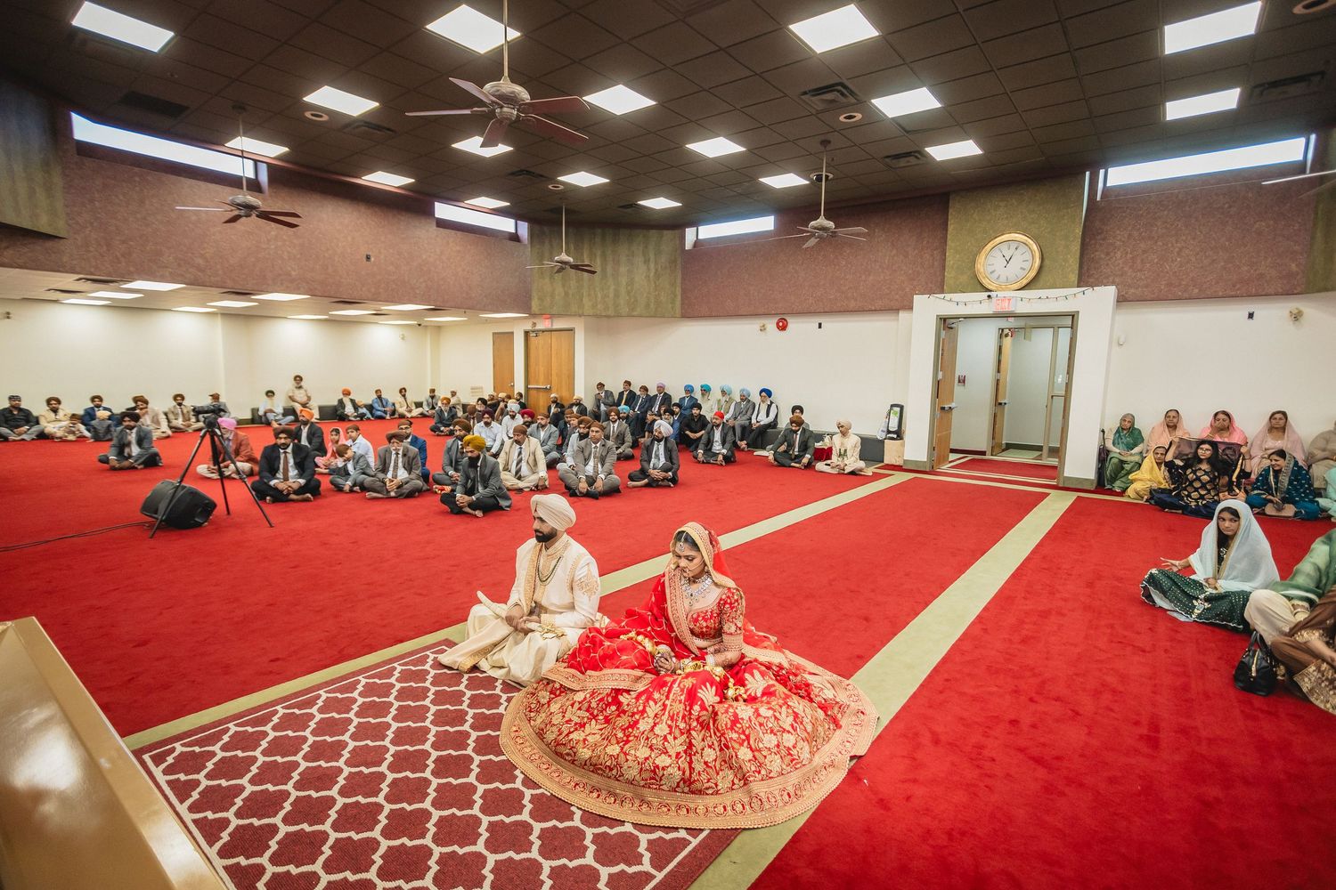 Panoramic view of traditional wedding ceremony in large hall with red carpeting.