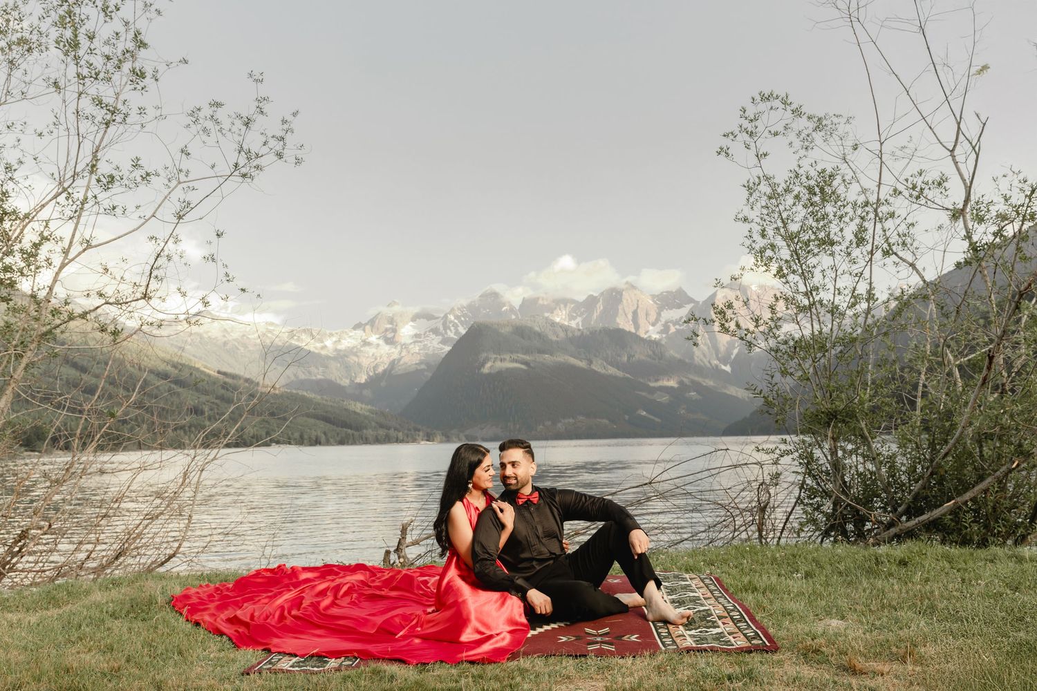 A romantic lakeside photo shoot featuring a flowing red dress against mountain scenery.
