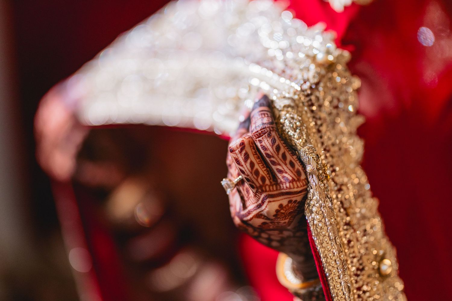 Close-up detail of intricate henna design and jewelry on hands during an Indian wedding ceremony.
