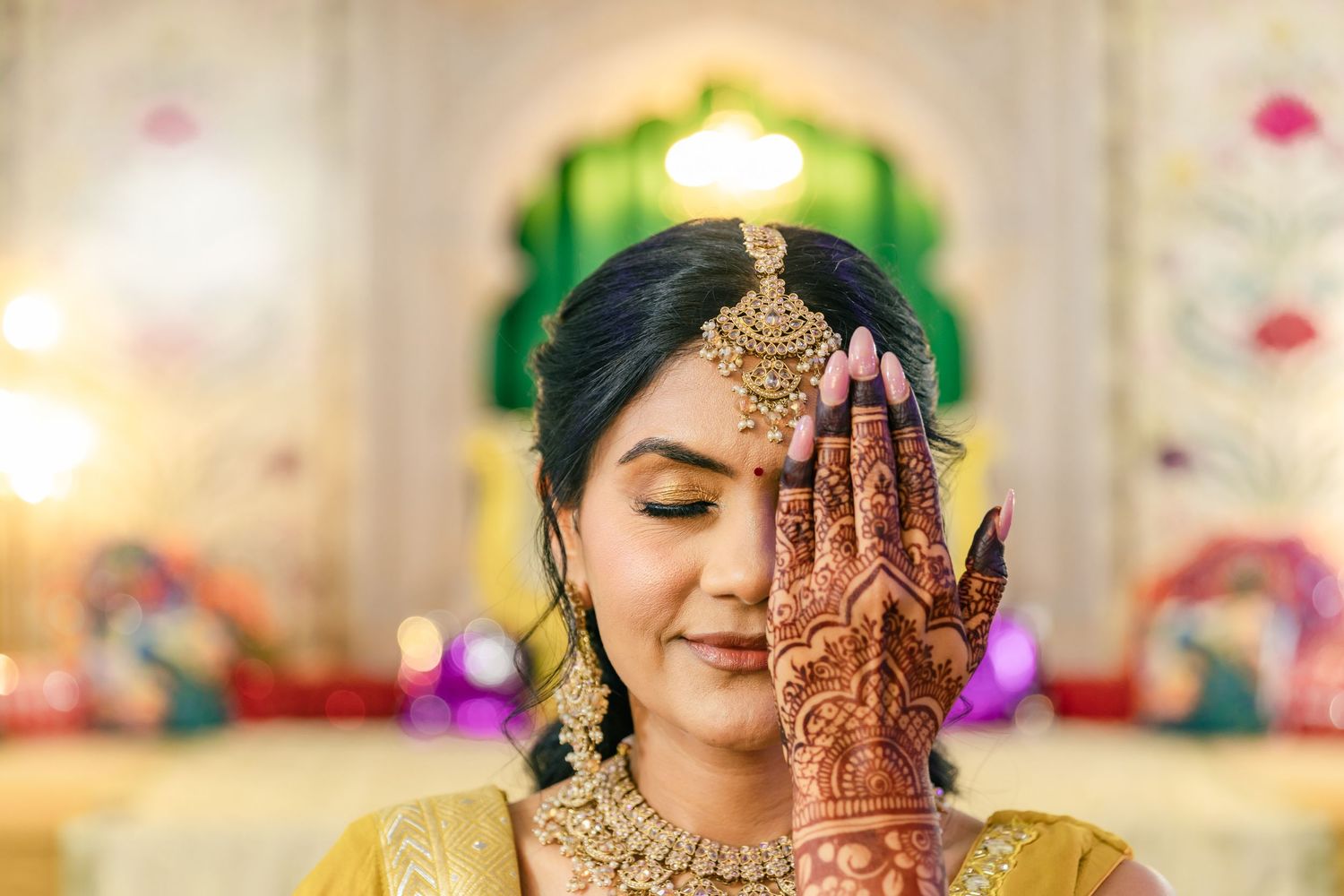 Traditional Indian bride wearing ornate gold jewelry and mehndi displays intricate henna designs in a celebratory pose.