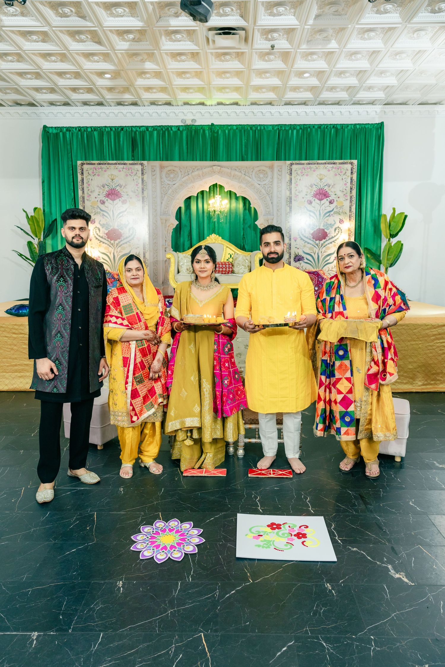 Wedding party group photo with people wearing yellow and red traditional outfits on black floor.