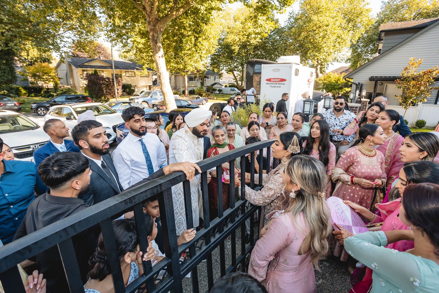 Outdoor wedding celebration with guests gathered under sunny tree canopy.