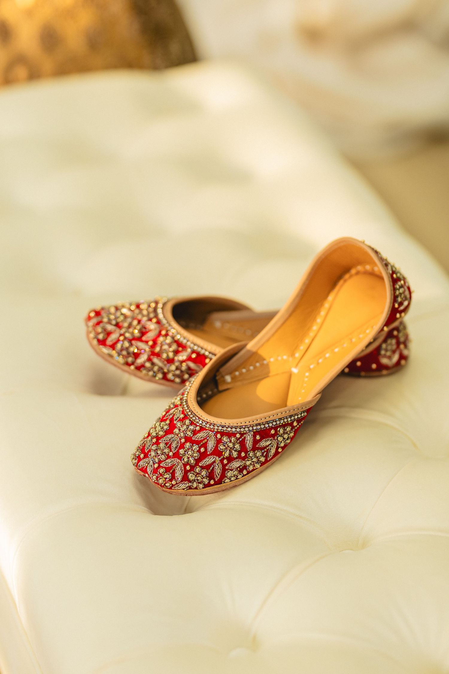 Traditional Indian wedding shoes with intricate red beadwork and embroidery details on gold leather.