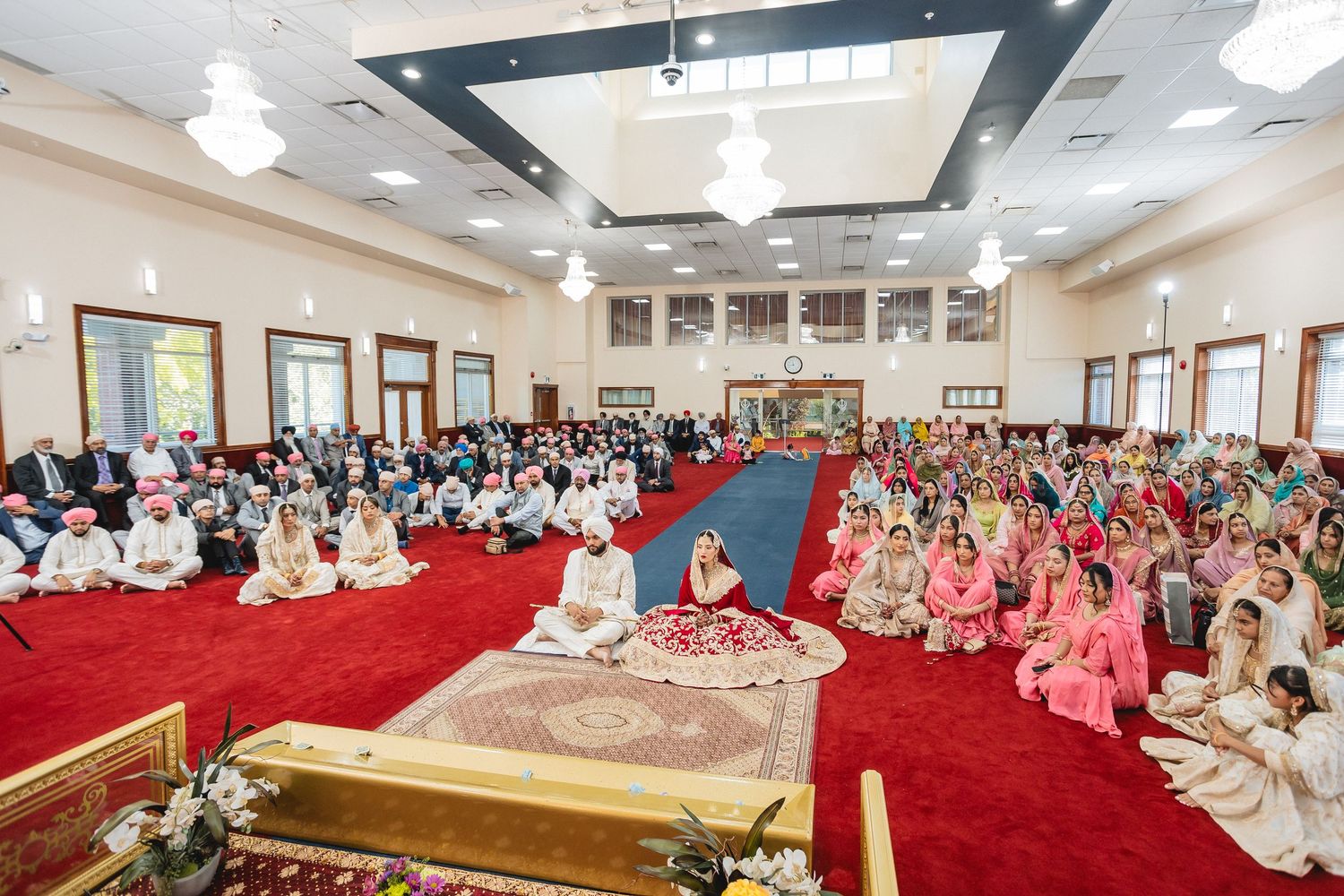Spacious banquet hall filled with guests seated on red carpet for traditional ceremony.