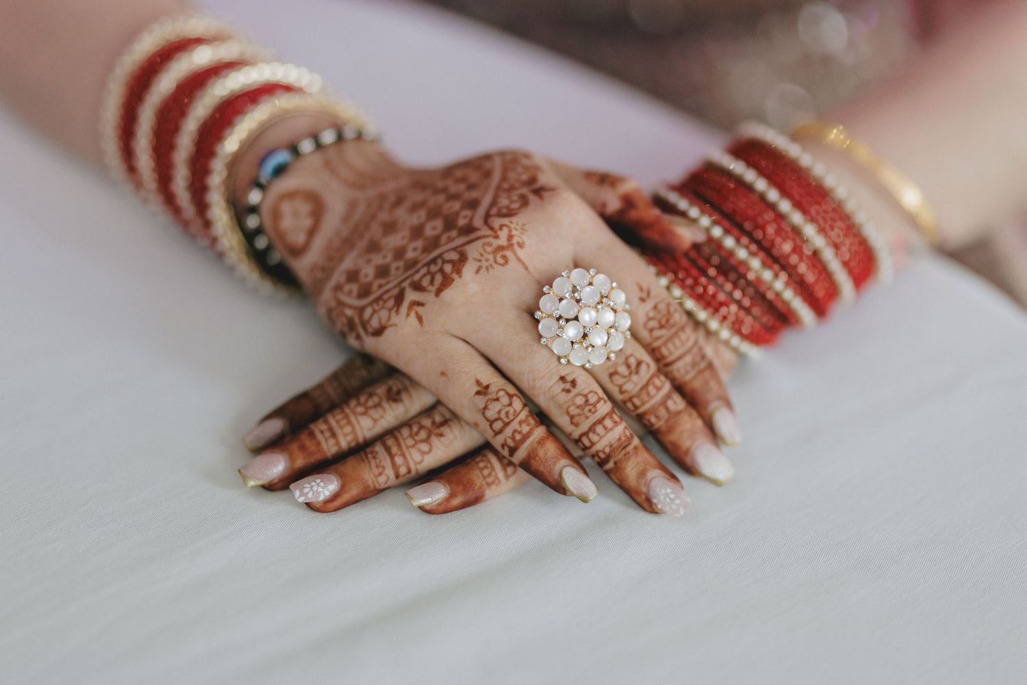 Close-up of intricate Mehndi designs on hands adorned with traditional bridal jewelry.