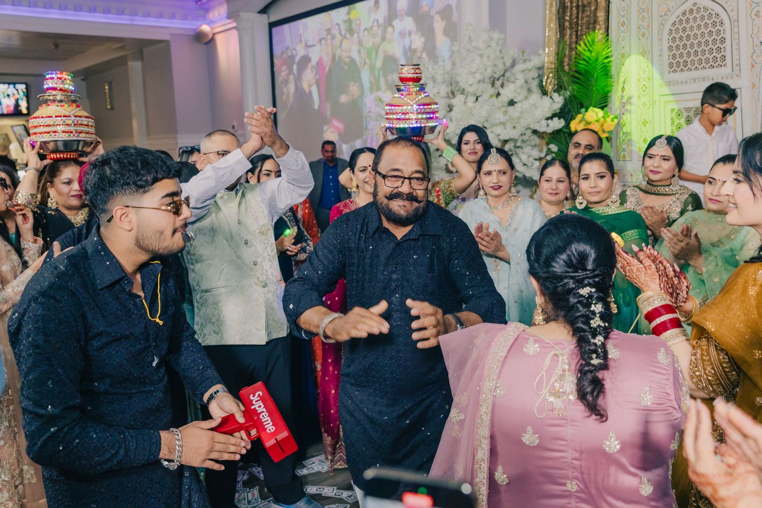 Energetic dance party scene at an Indian wedding reception with colorful lighting and decor.