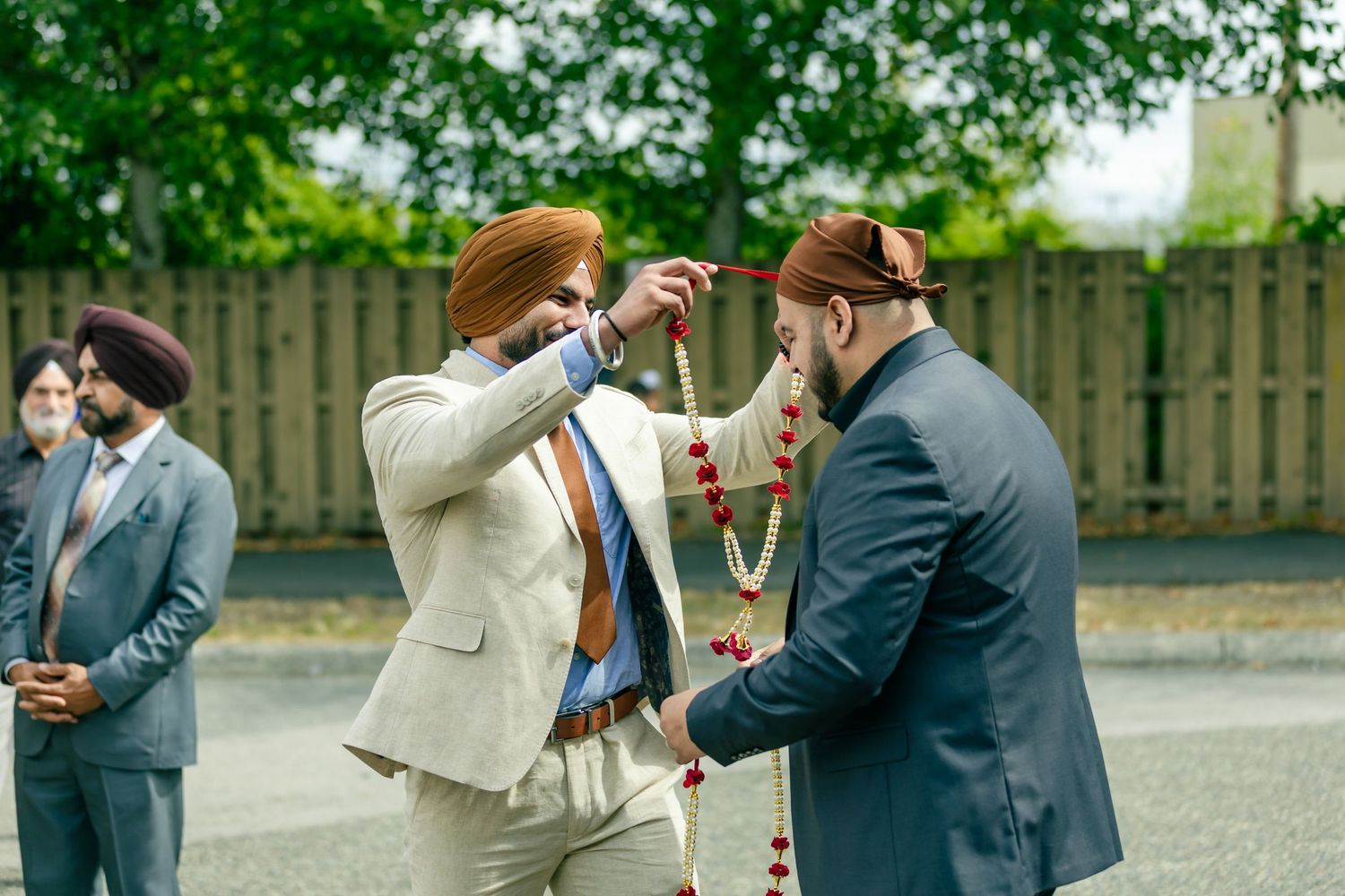 A group of people in formal attire interact and check their phones while standing outdoors.
