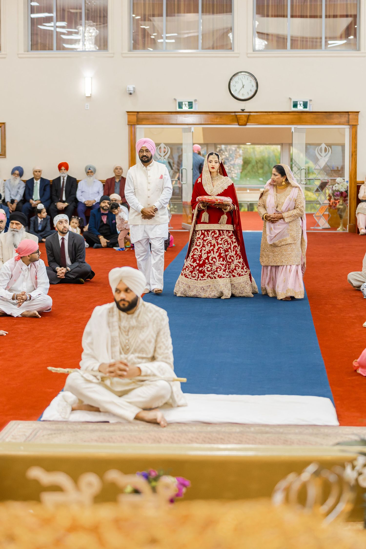 Traditional Sikh wedding ceremony in progress with guests seated on floor in temple hall.