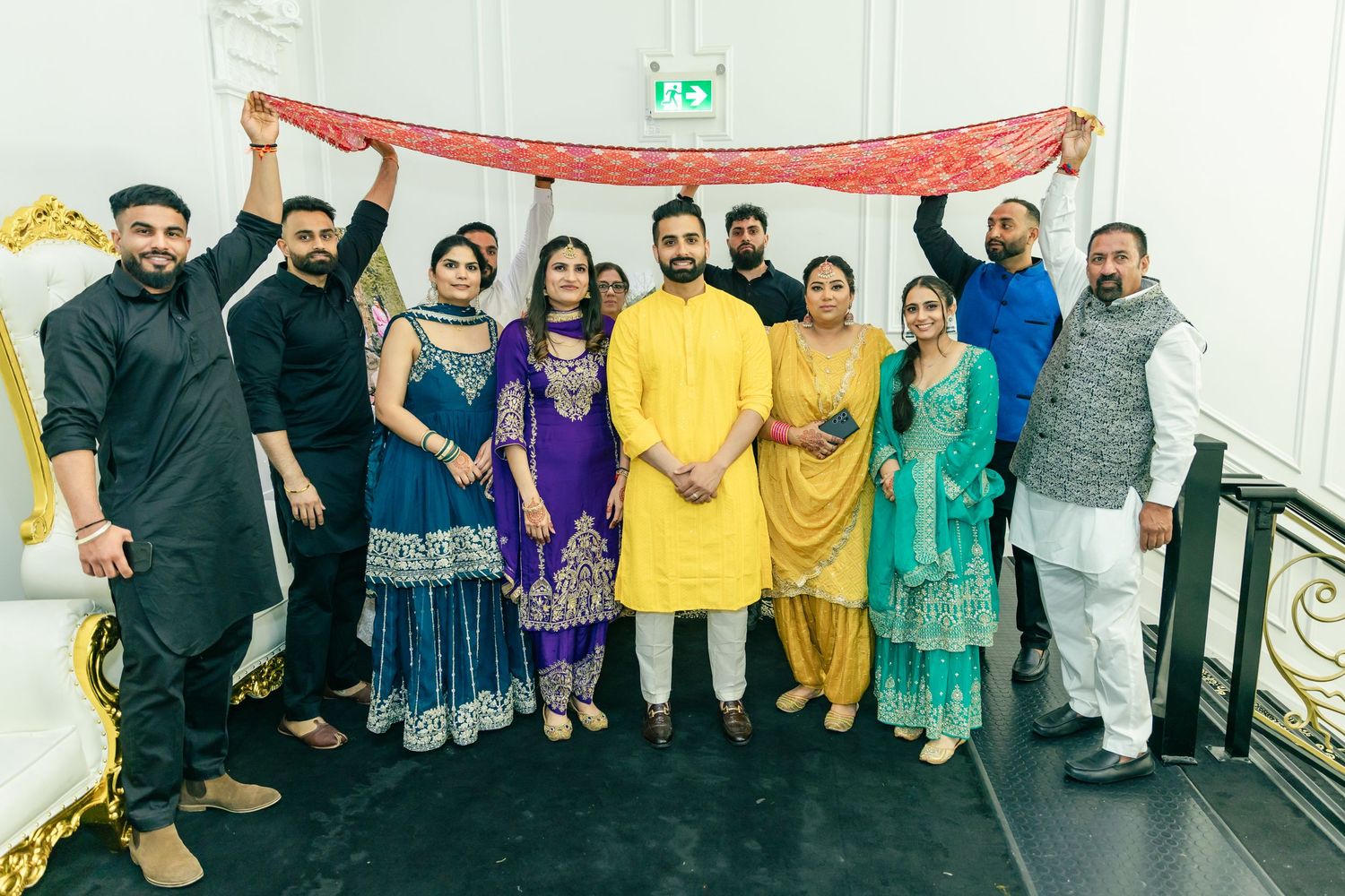 Large group photo of wedding guests wearing traditional Indian attire in yellow and purple standing together.