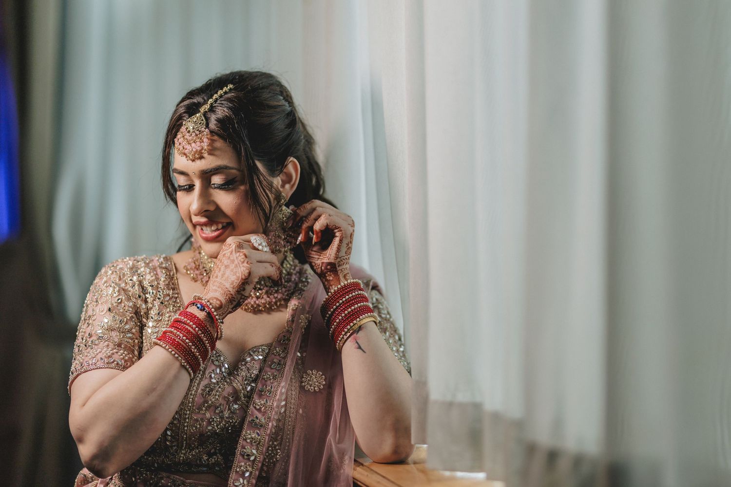 A bride in an ornate red and gold lehenga poses during a traditional Indian wedding celebration.