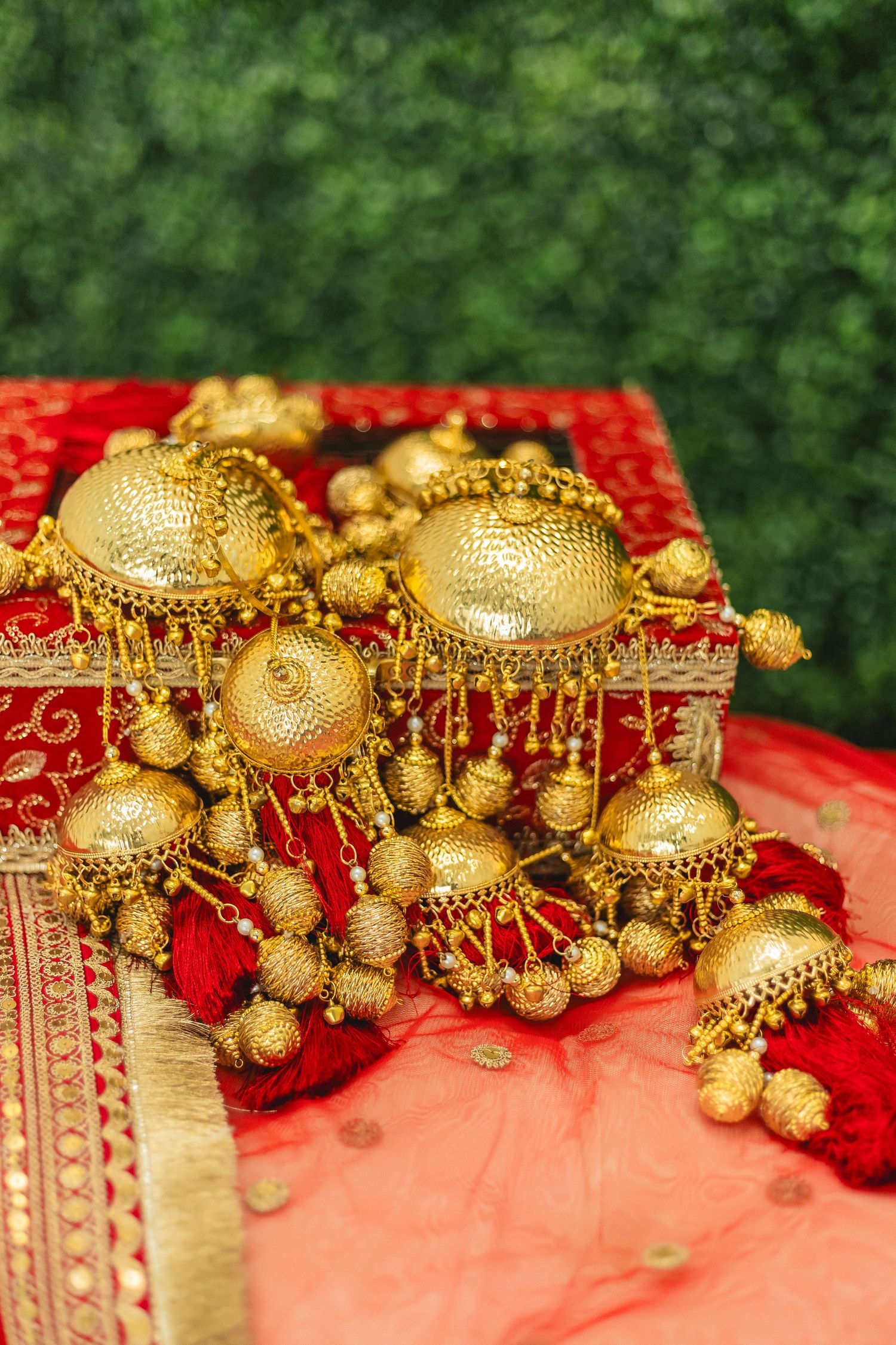 Traditional Indian gold jewelry kaliras with intricate designs and bells displayed on red fabric.