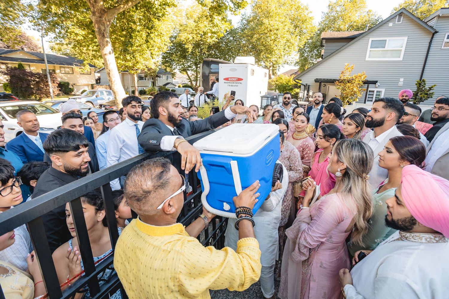 Crowd gathered outdoors around blue cooler during festive celebration.