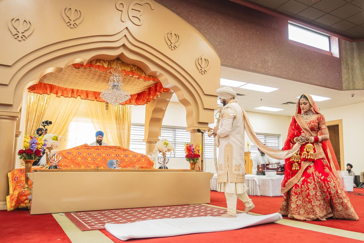 Wide angle view of traditional wedding ceremony space with decorative arches and red carpet.