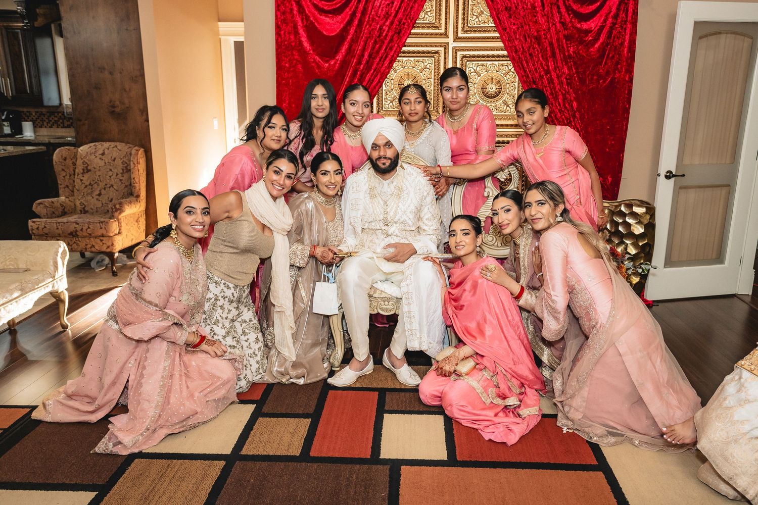 A group in coordinated pink and peach formal attire poses together at an elegant indoor celebration.