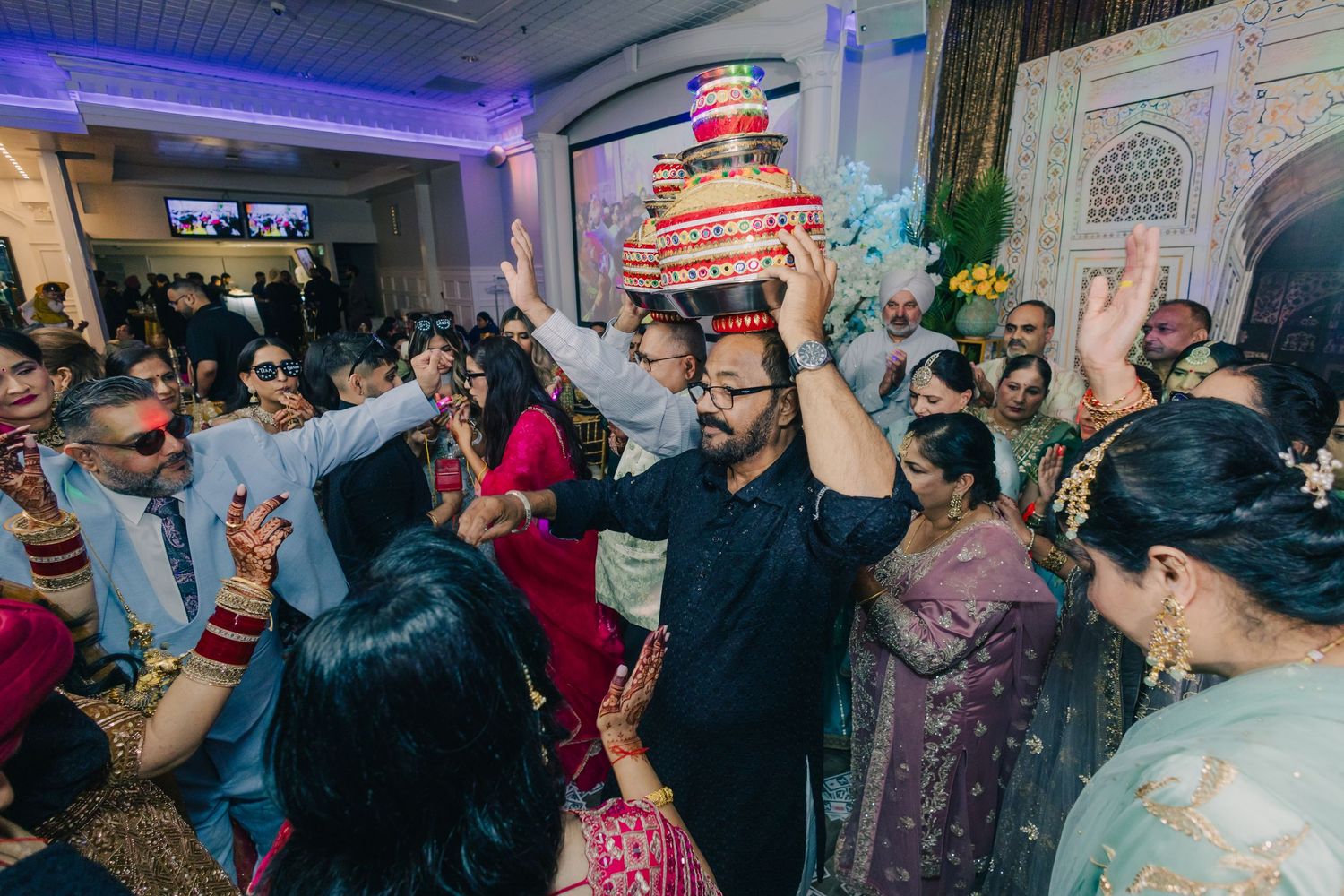 Lively wedding reception party with guests dancing under purple lighting in a decorated venue.